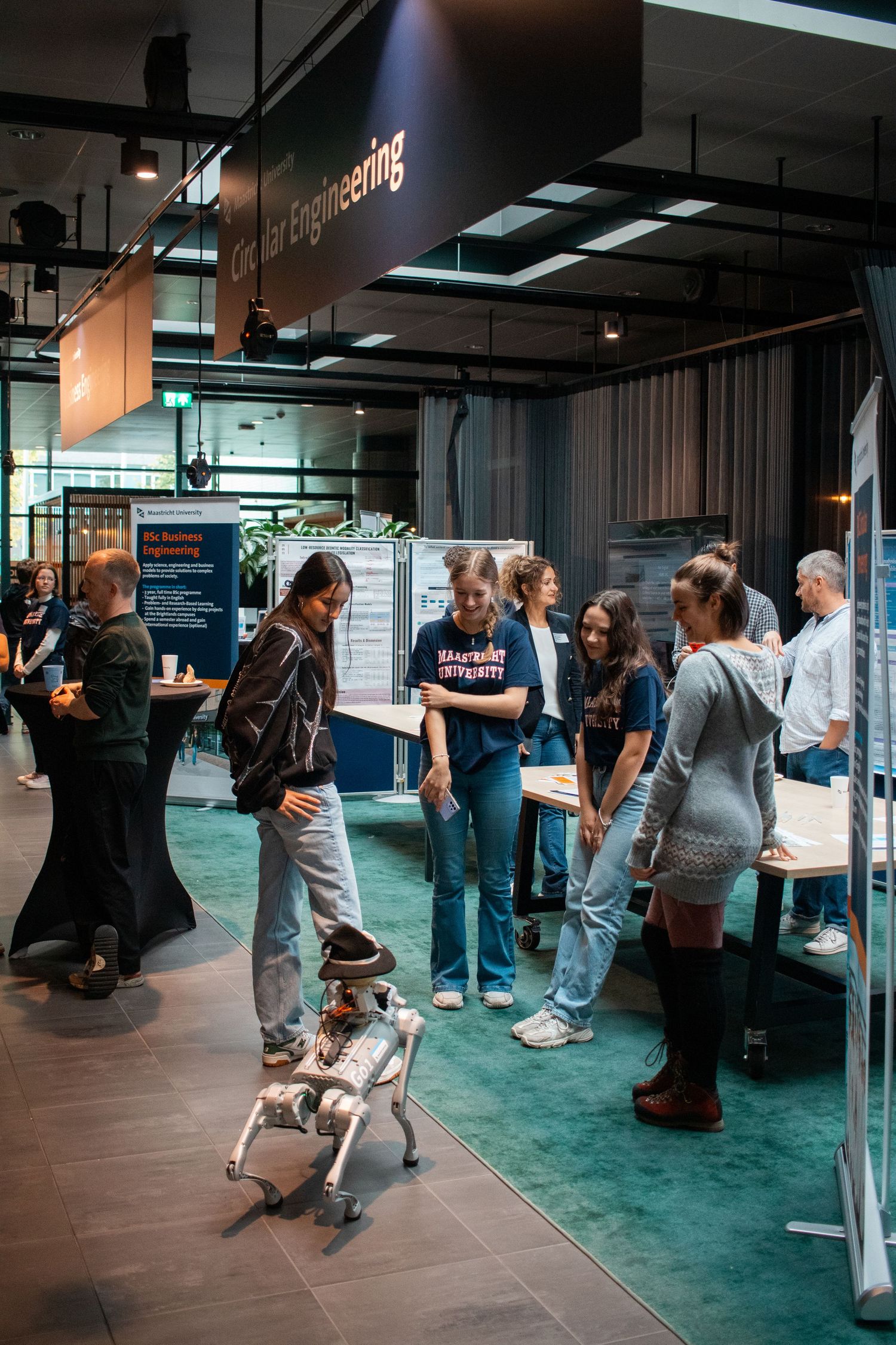 Students gathered around a robotic dog at a university engineering department open day exhibition.