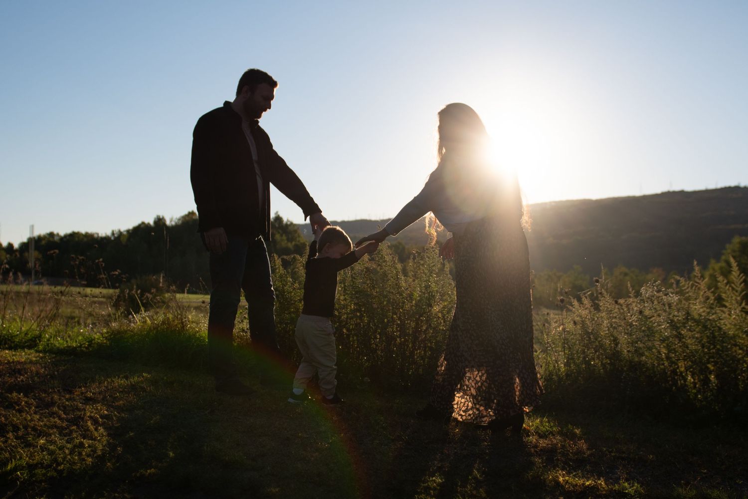 Silhouette of a family with a young child holding hands in a sunlit field at golden hour.