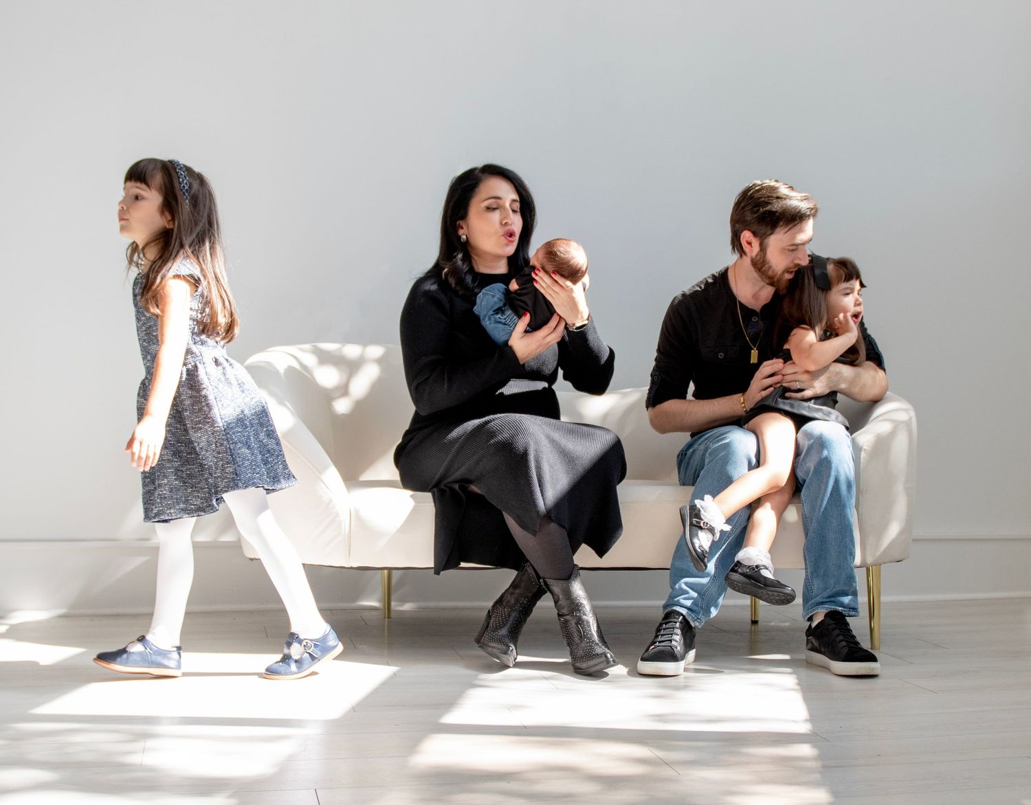 Family portrait with mother holding baby, father with child, and daughter standing in bright white studio.
