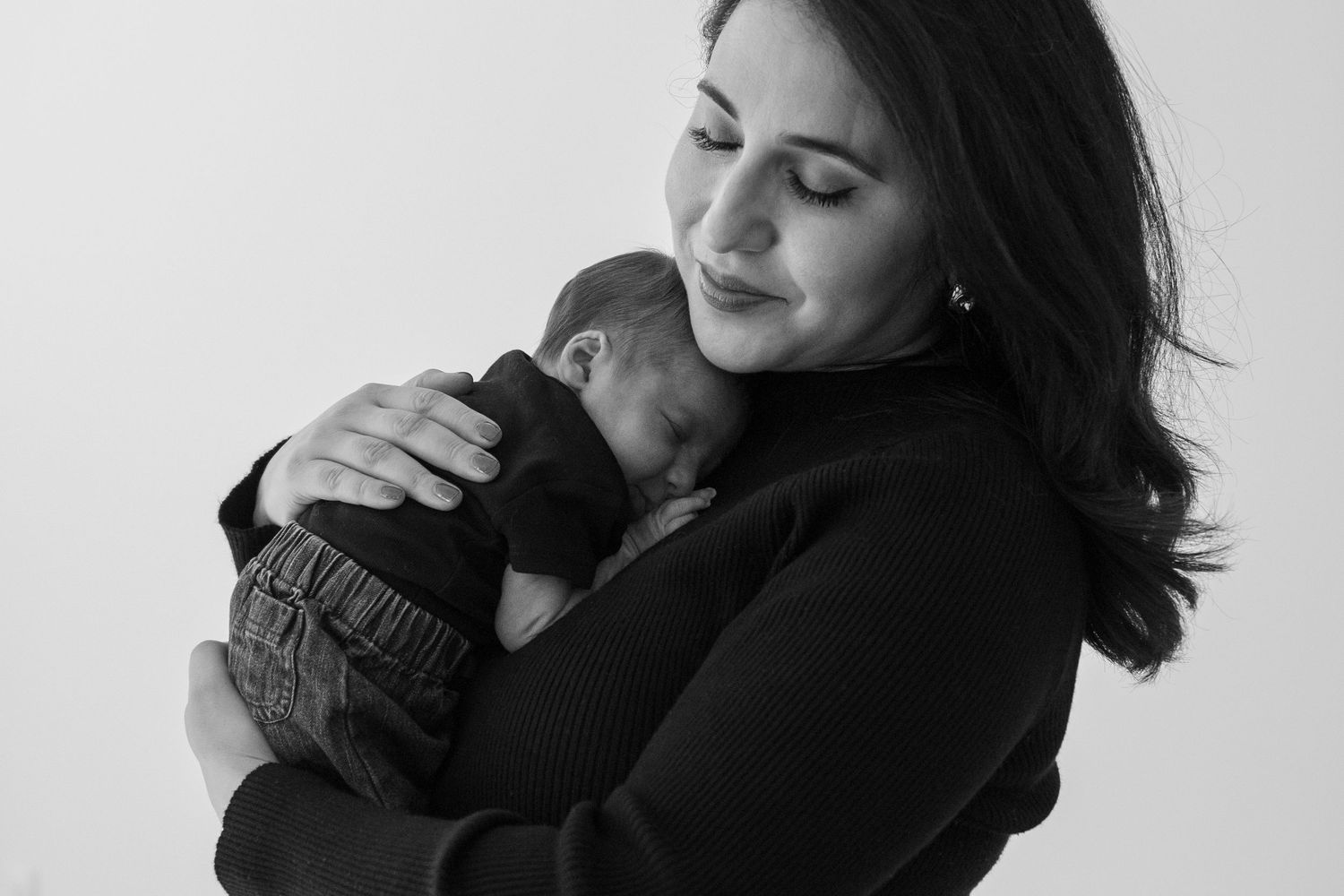 Black and white portrait of mother tenderly holding and cuddling her sleeping newborn baby.