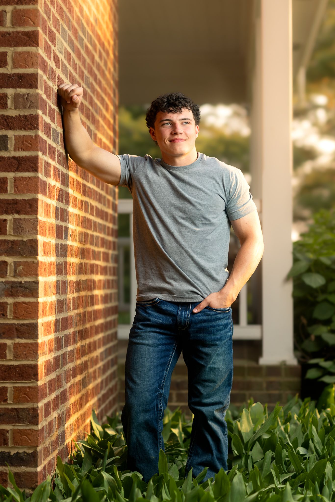 Golden hour high school senior in Delafield, Wisconsin. Teen boy leaning on brick, smiling, captured in warm, joyful photography.