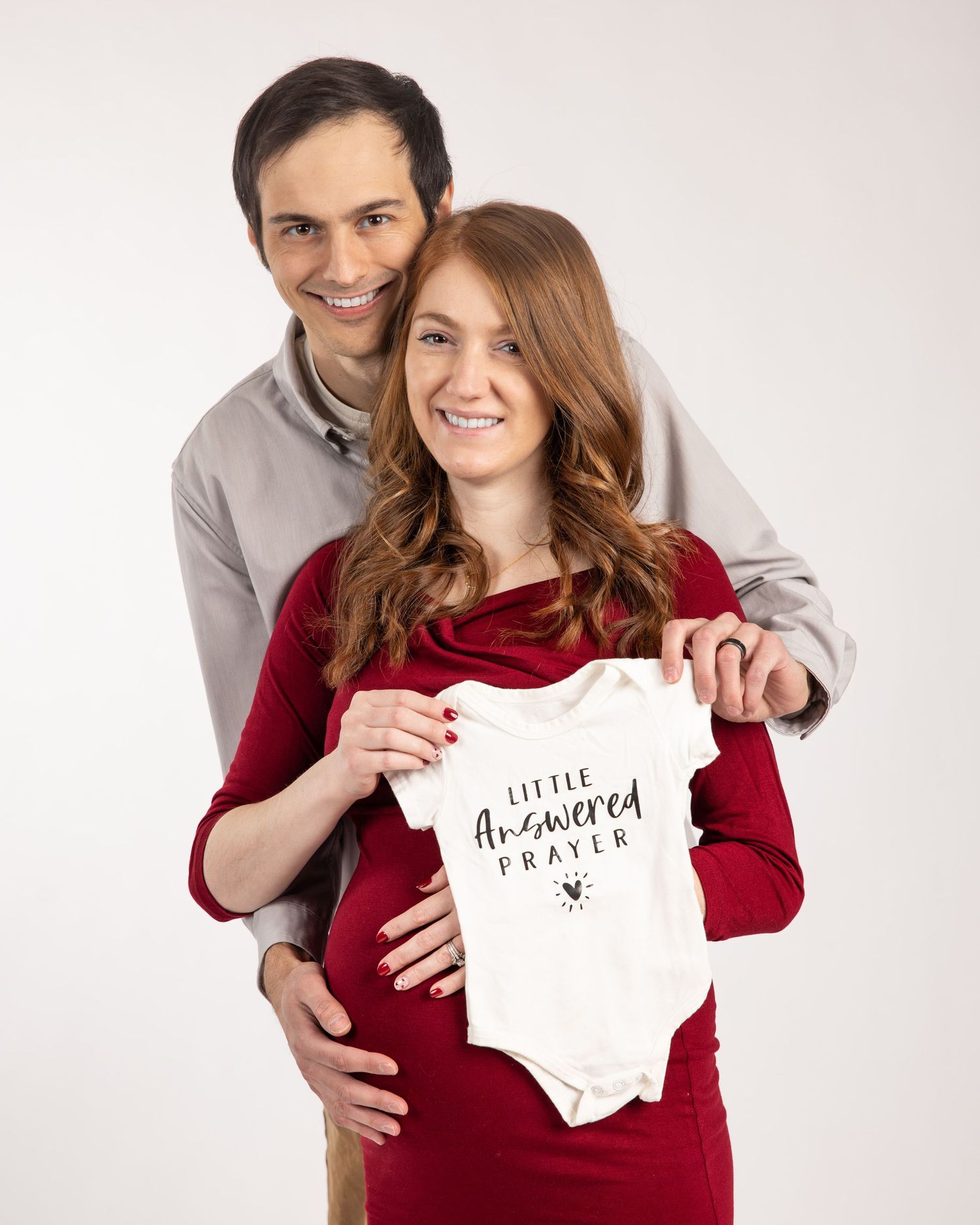 Husband and wife Maternity, holding onsie and excited for their new baby to arrive.  Waukesha, WI.  Expecting parents and in love.