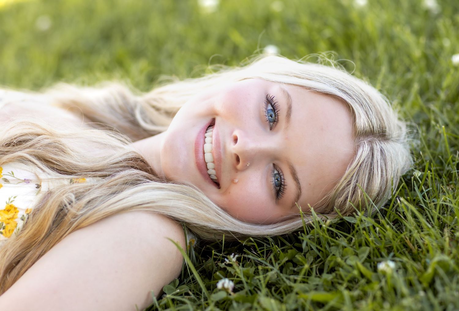 Port Washington senior photography. Teen girl with blonde hair and blue eyes laying in grass, creating timeless, elegant highschool portrait