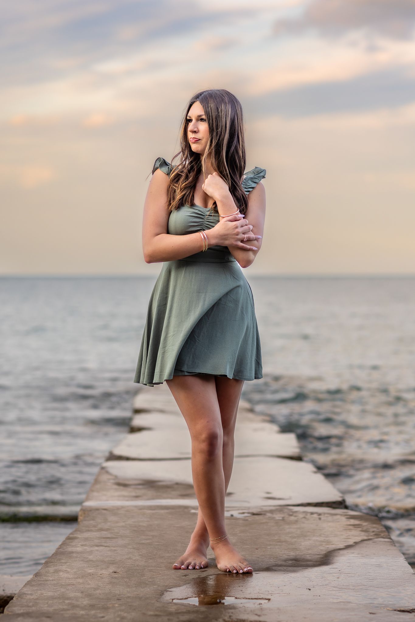 Whitefish Bay senior photography by Lake Michigan. Teen in a green dress on rocks, with wind-blown hair, creating moody, natural portraits.
