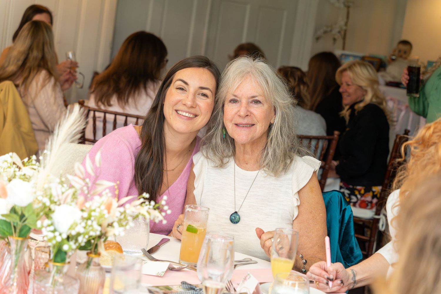 Guests enjoying refreshments and conversation at an elegant baby shower luncheon with floral centerpieces.
