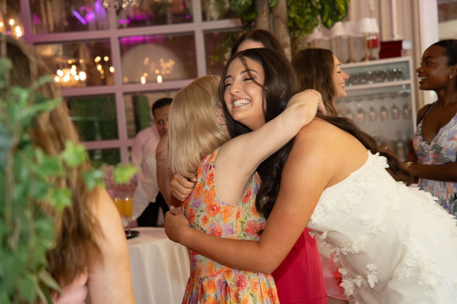 Friends share an emotional embrace during a celebration with festive decor in the background.