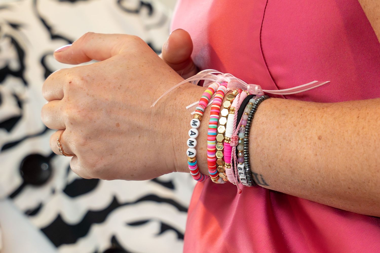 Colorful beaded bracelets and bangles stacked on a wrist against a patterned background.