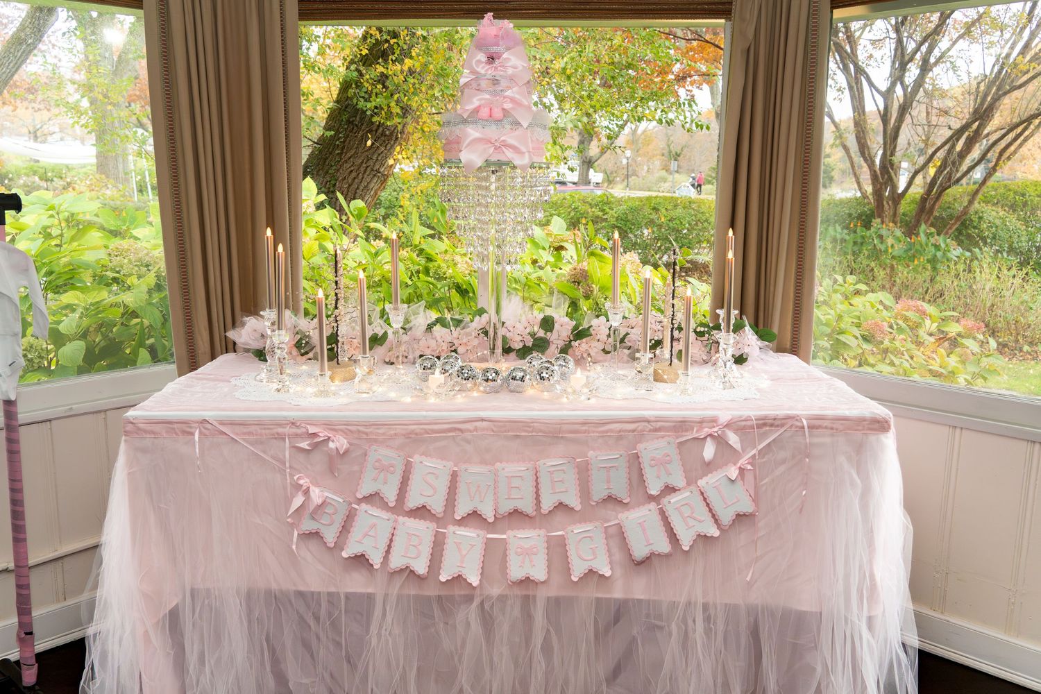 Baby shower decorations with pink tulle and banners adorn tables in a sunlit room.