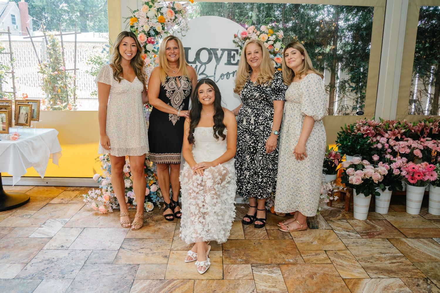 Guests gather for photos at a bridal celebration with floral wall decor.