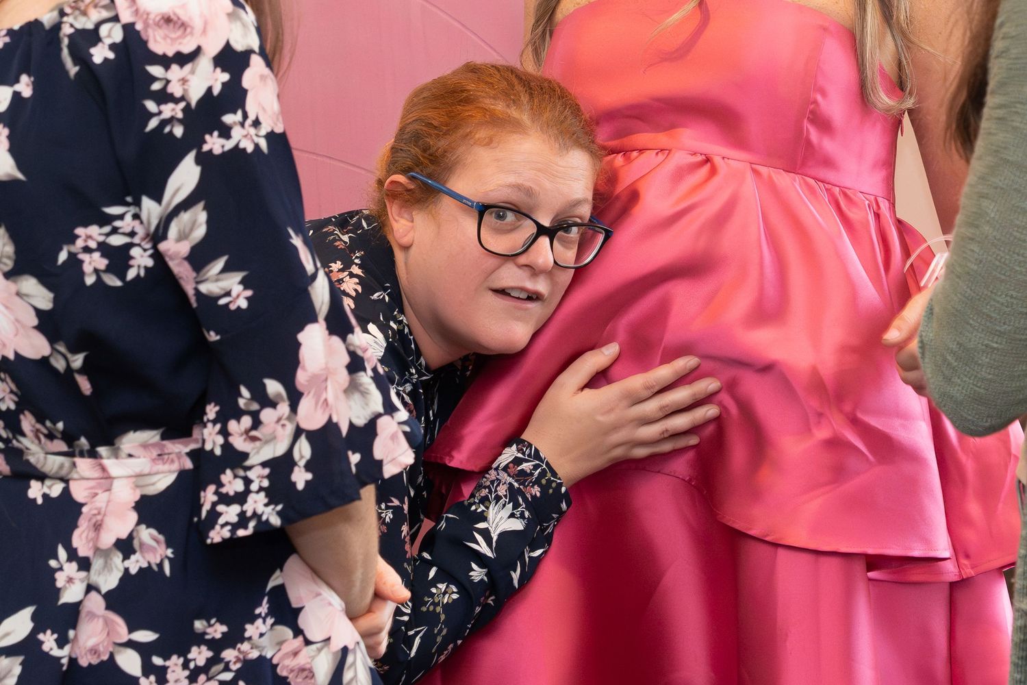 A guest in a floral dress shows excitement at a pink-themed baby shower celebration.