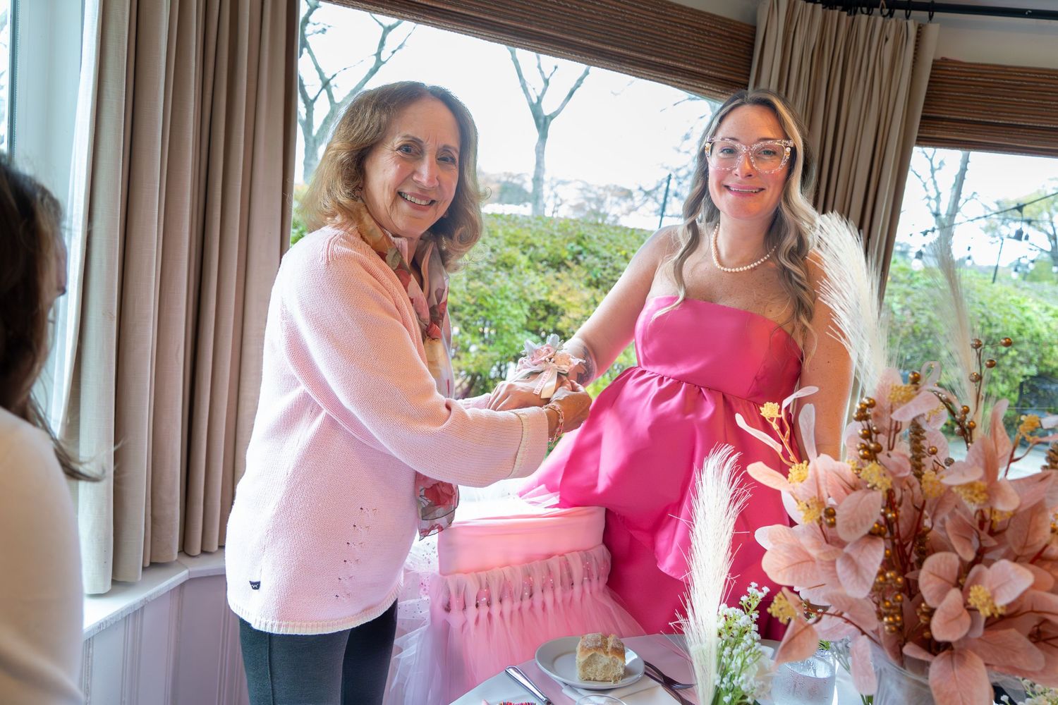 Two guests share a joyful moment at a baby shower celebration with pink decor and floral arrangements.