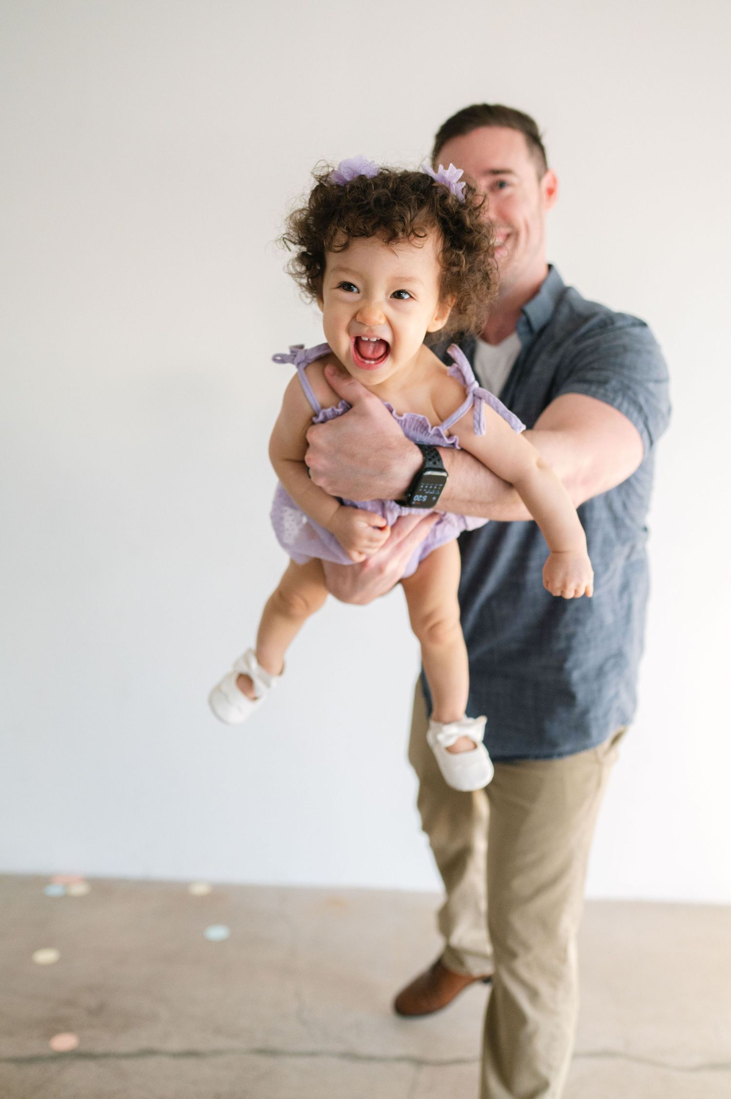 A series of four playful photos showing a parent lifting and spinning a laughing baby in a white dress.