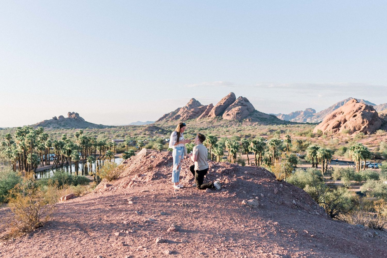 Panoramic desert landscape with red rock formations and mountains stretching across the horizon at sunset.