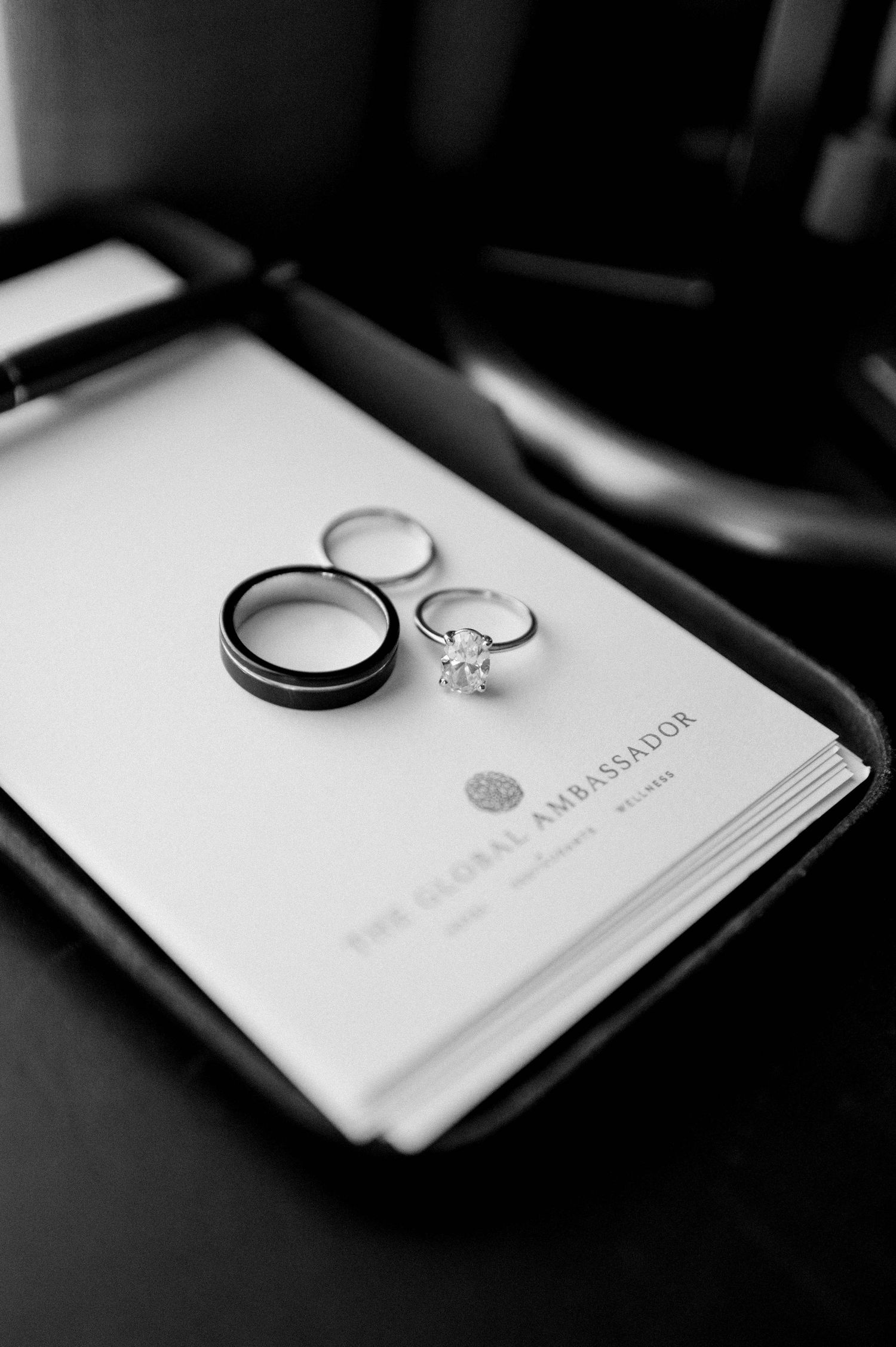 Black and white photo of wedding rings resting on a document, showing an engagement ring and two wedding bands.