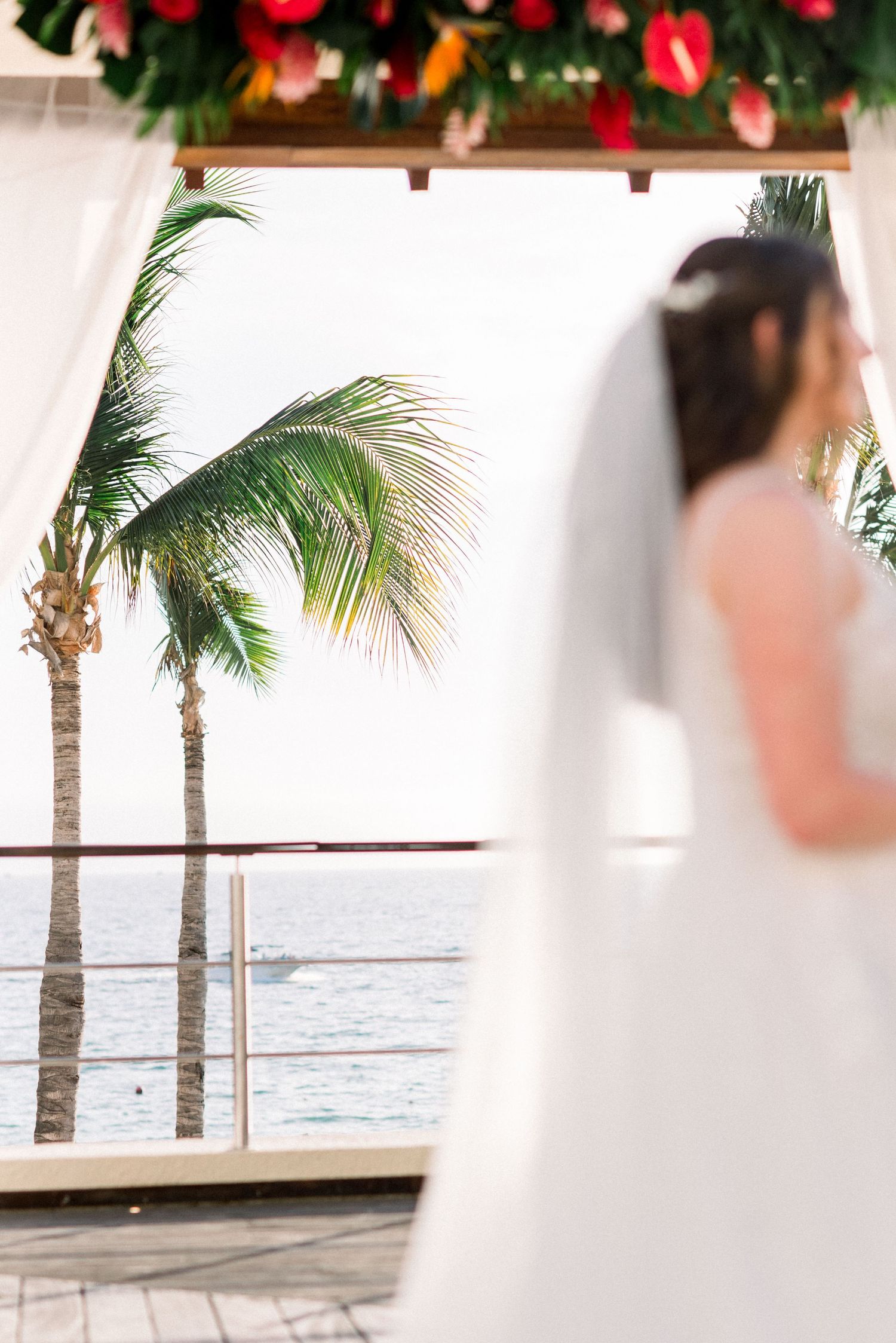 Palm trees frame a beachside wedding ceremony with tropical ocean views and floral decorations.