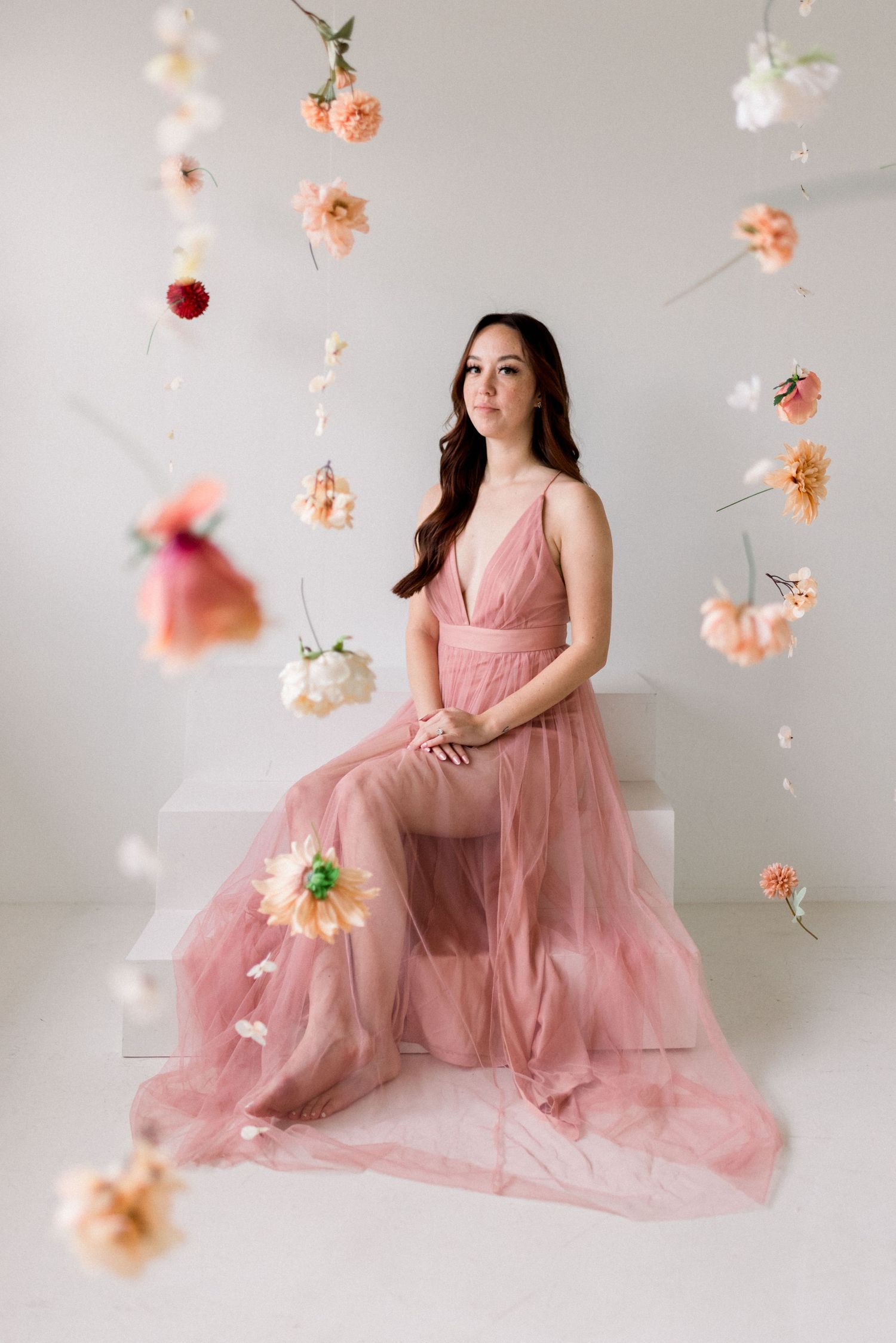 A dreamy portrait with floating peach roses and woman in pink tulle gown against white backdrop.