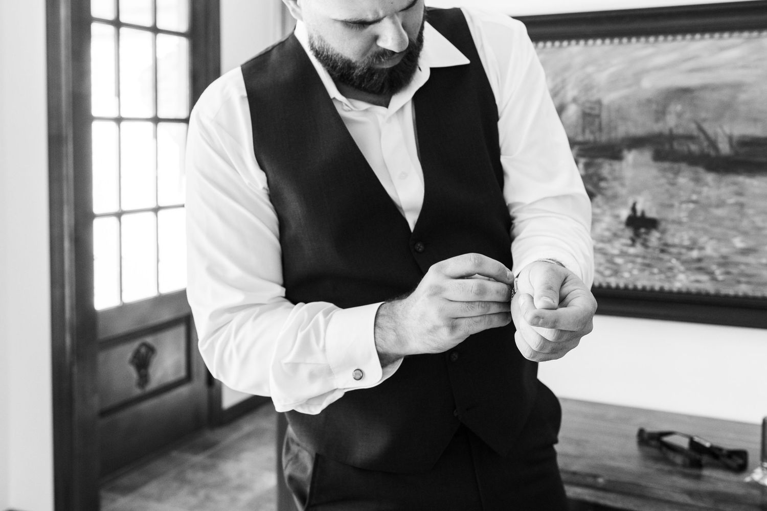 Close up of groom fastening cuff buttons during wedding preparation in black and white.