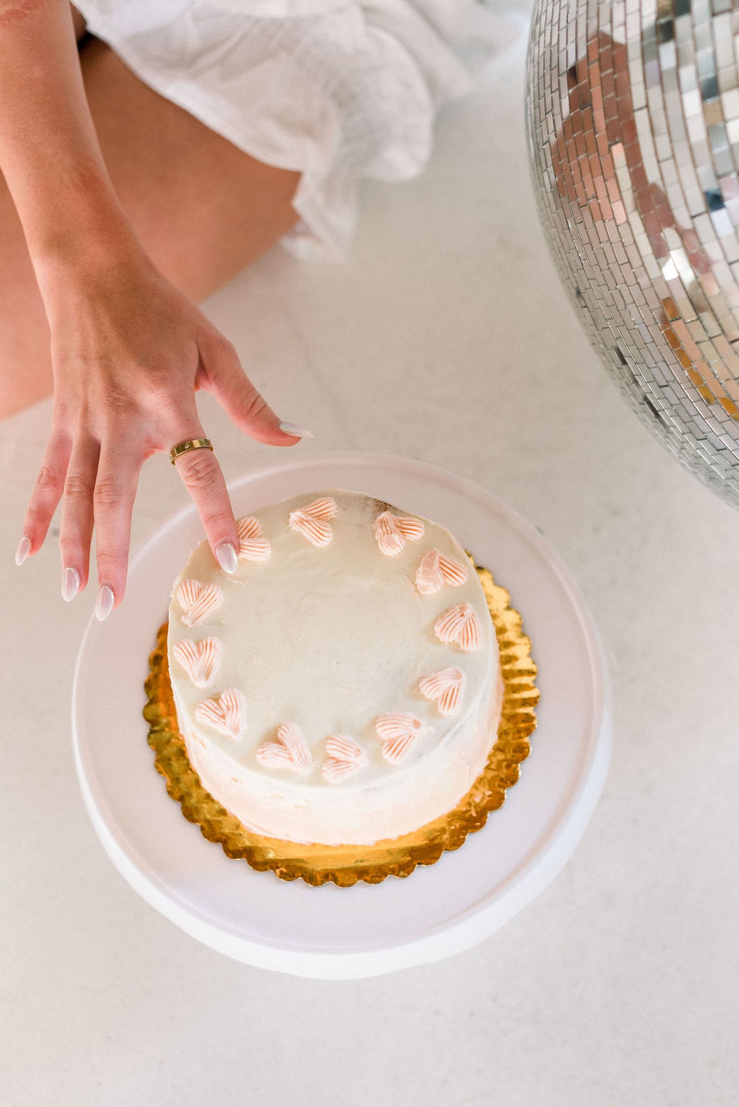 Hand reaching for elegant white cake with pink piping details on white cake stand.
