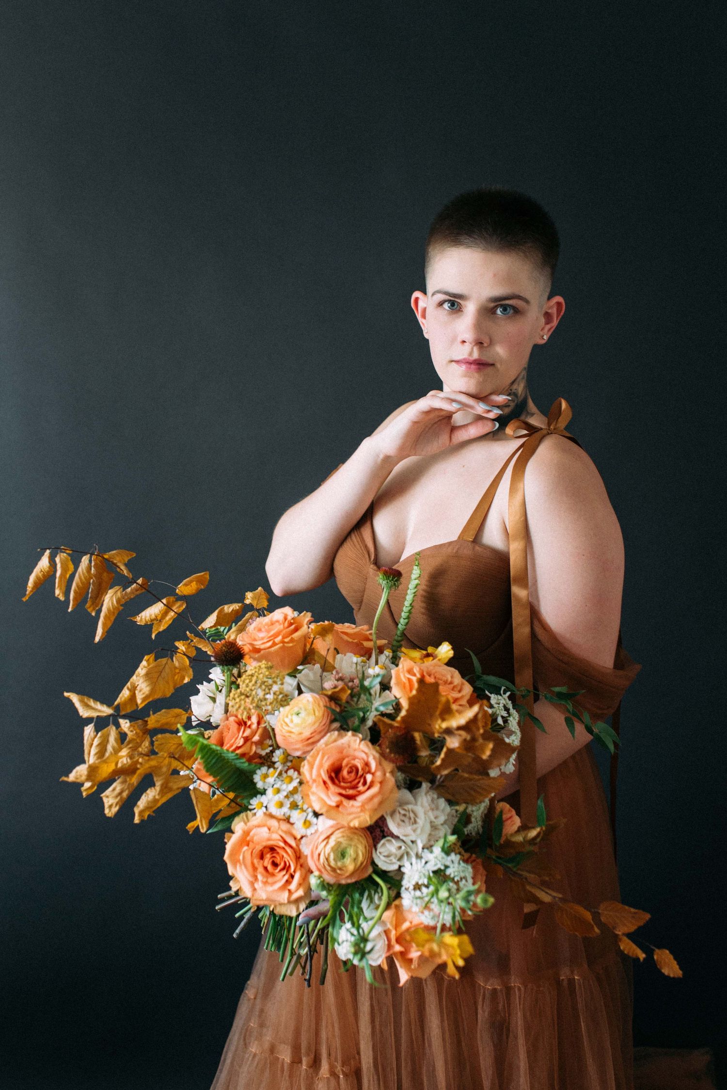 Studio portrait with elegant peach and orange floral bouquet against dark background.