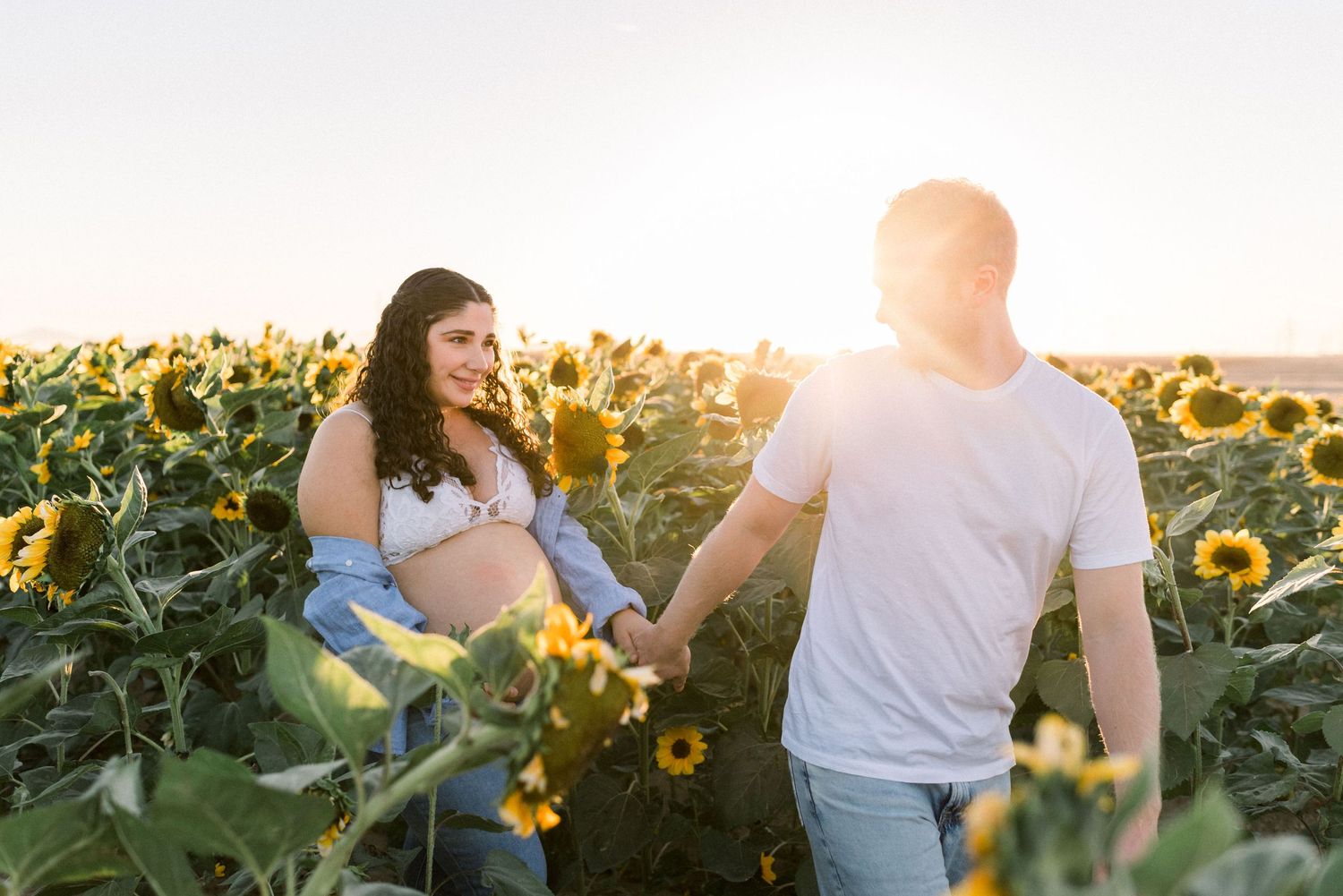 Maternity photo of couple walking in sunflower field