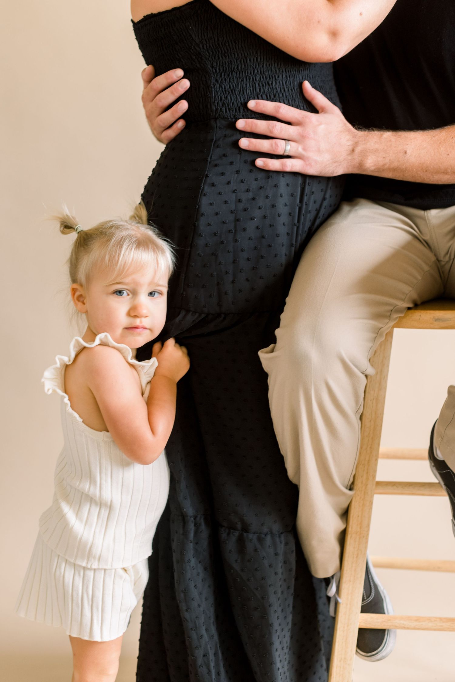Child in white dress embracing parent wearing black dress during photo session.