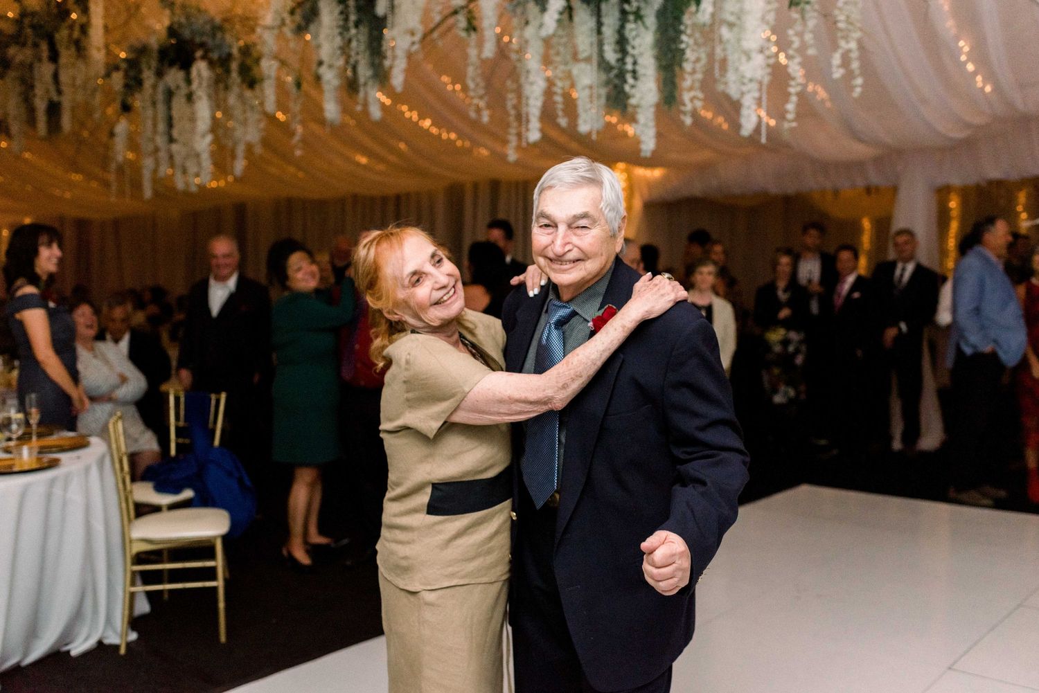 Couple dancing together at an elegant wedding reception under draped fabric and hanging floral decorations.