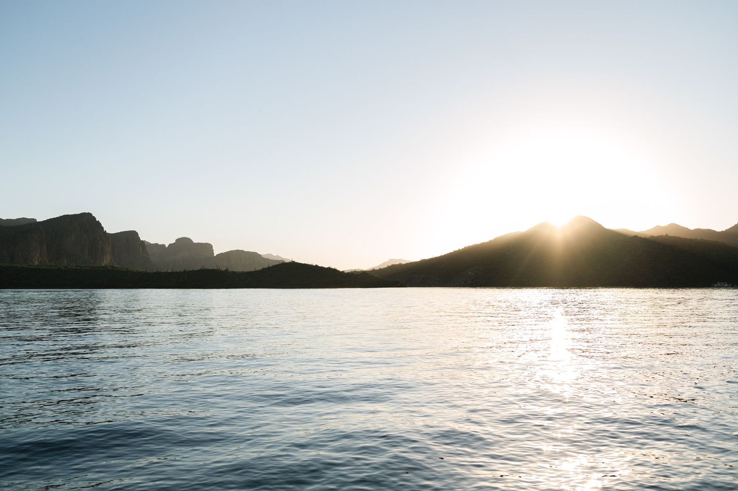Panoramic mountain landscape with sun setting over a tranquil lake.