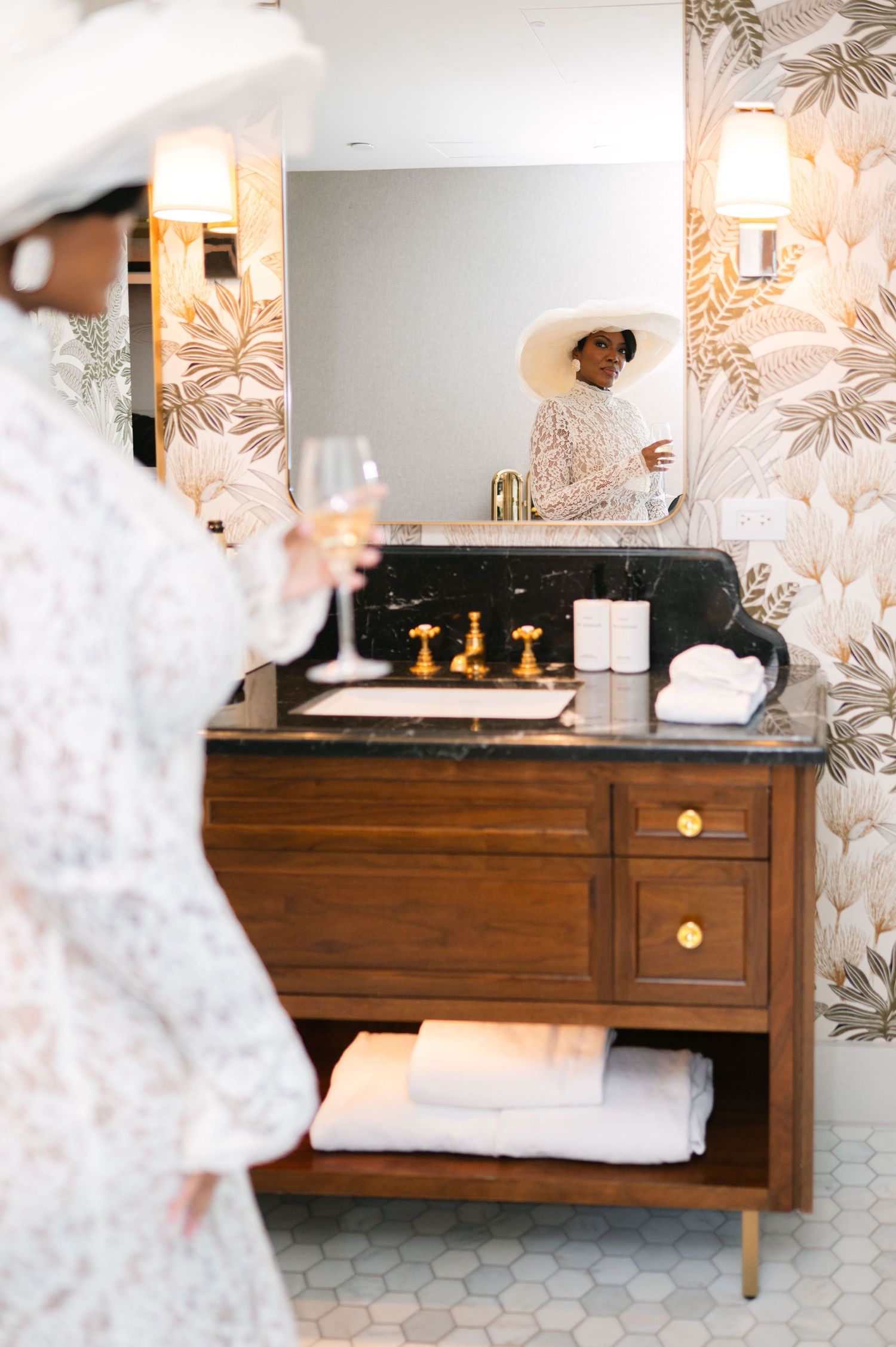 Mid-century modern wooden dresser with white bedding and floral wallpaper in an elegant bedroom setting.