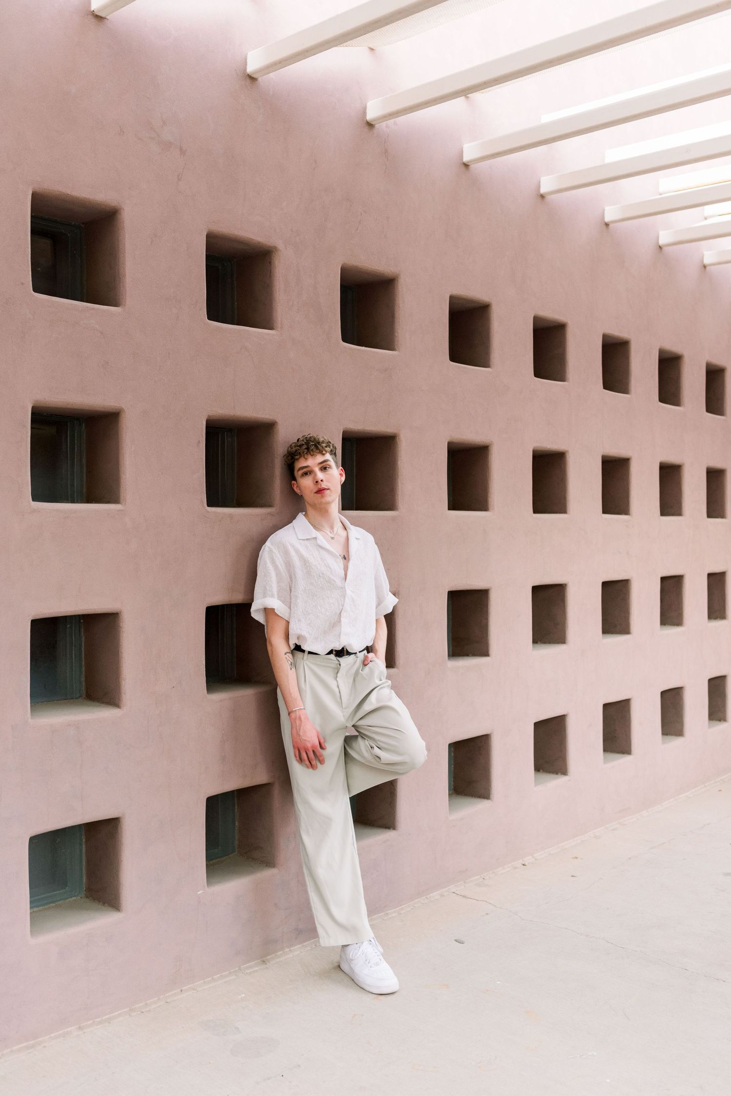 Fashion portrait against modern architectural wall with square cutouts and dramatic lighting.