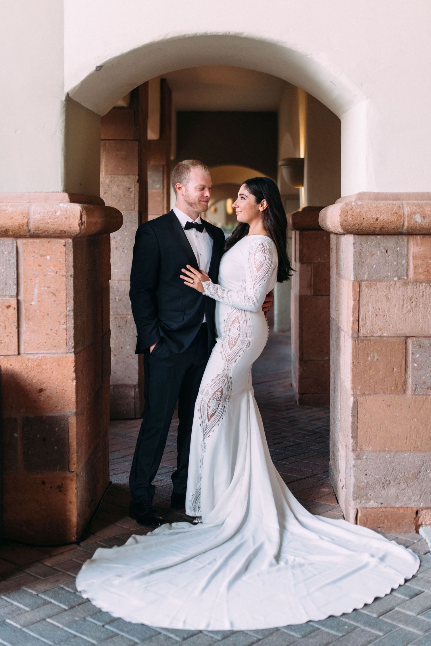 A romantic wedding portrait under a stone archway showcases the bride's elegant lace gown.