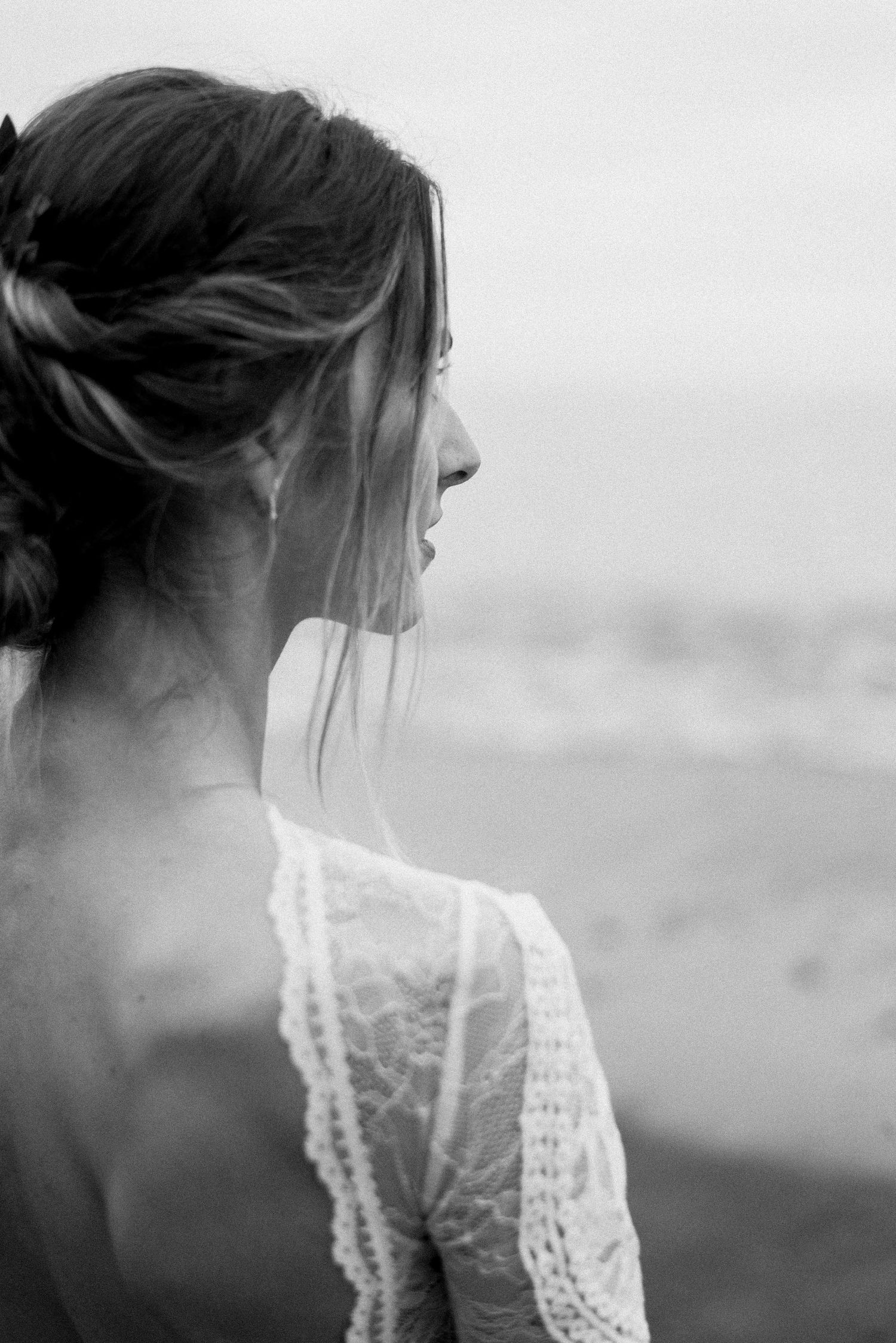 Black and white profile of a bride with delicate lace detail and windswept updo.