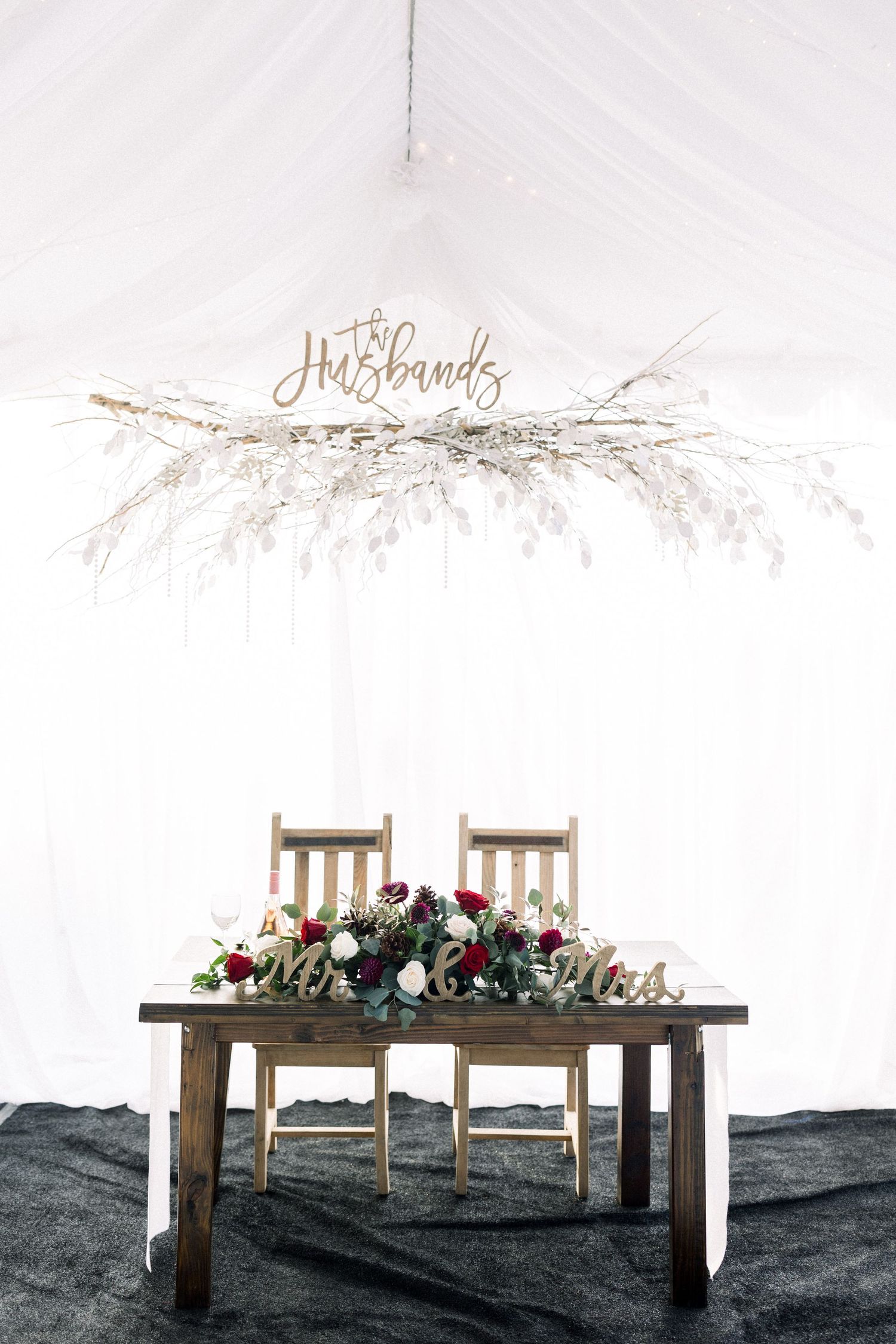 Rustic sweetheart table with floral arrangement and 'Mr & Mrs' sign overhead.