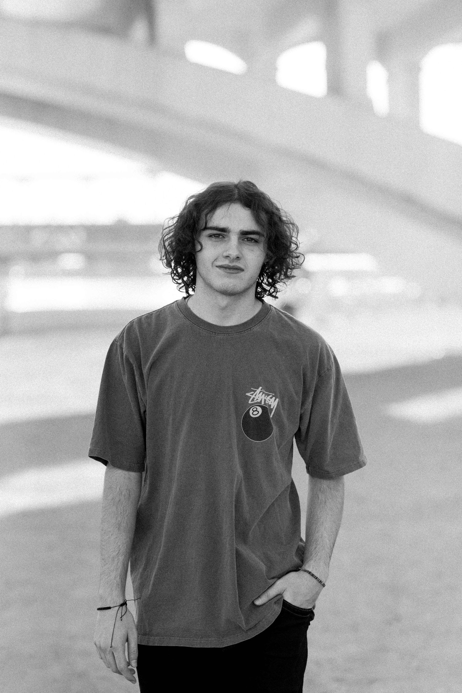 Casual portrait of person in gray t-shirt with curly hair against blurred architectural background.