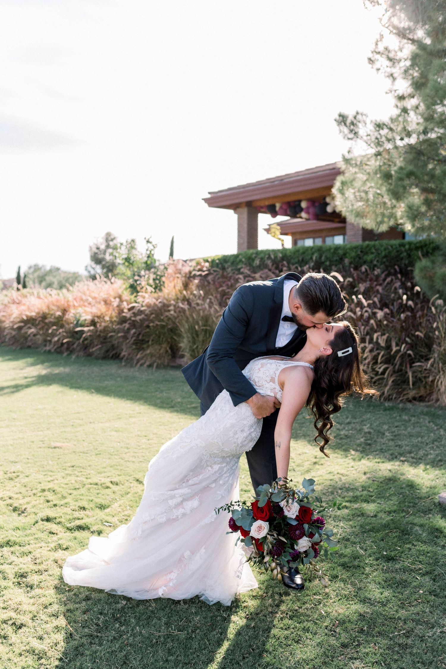 Romantic dip kiss between newlyweds on manicured lawn with architectural backdrop.