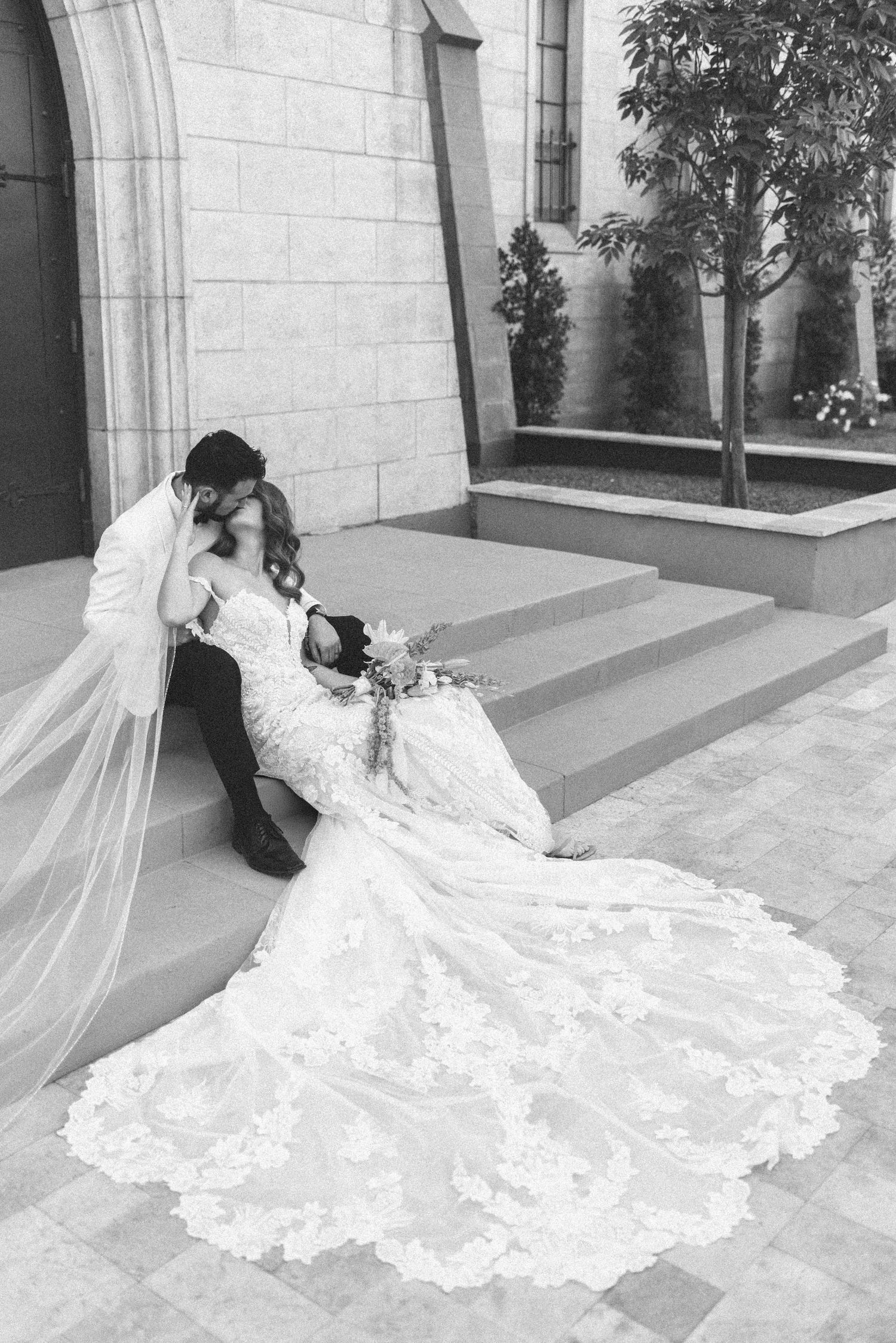 Elegant white lace wedding dress with long train sprawled across stone patio.