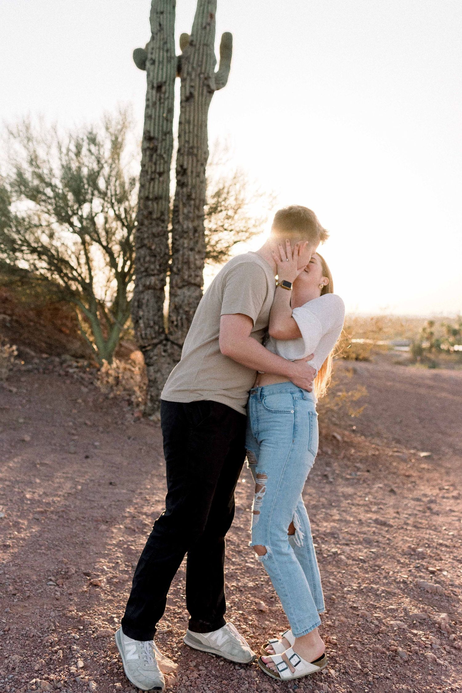 A couple shares a romantic moment in front of desert cacti during golden hour sunset.