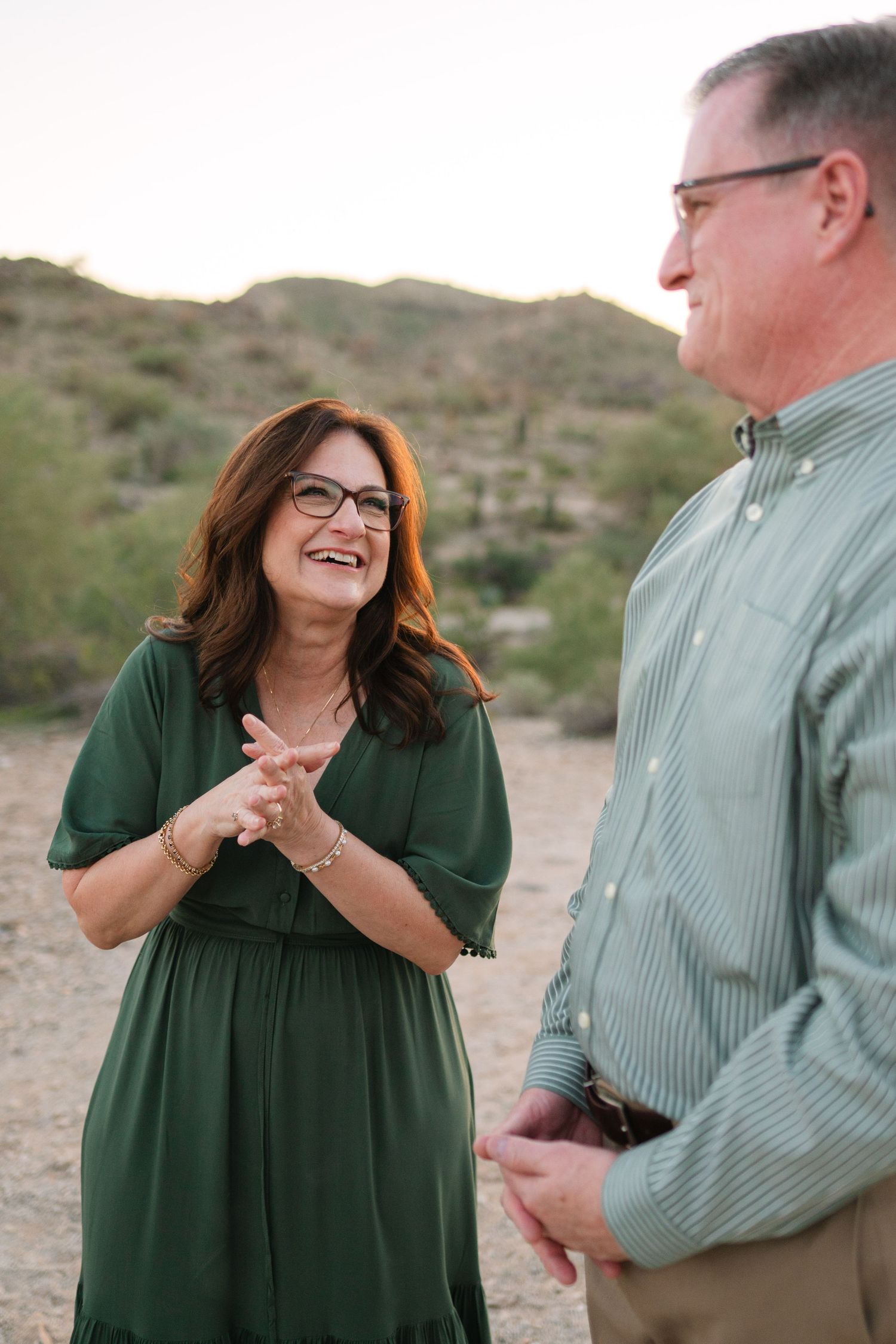 A couple shares joyful laughter together while posing outdoors in a desert landscape at sunset.