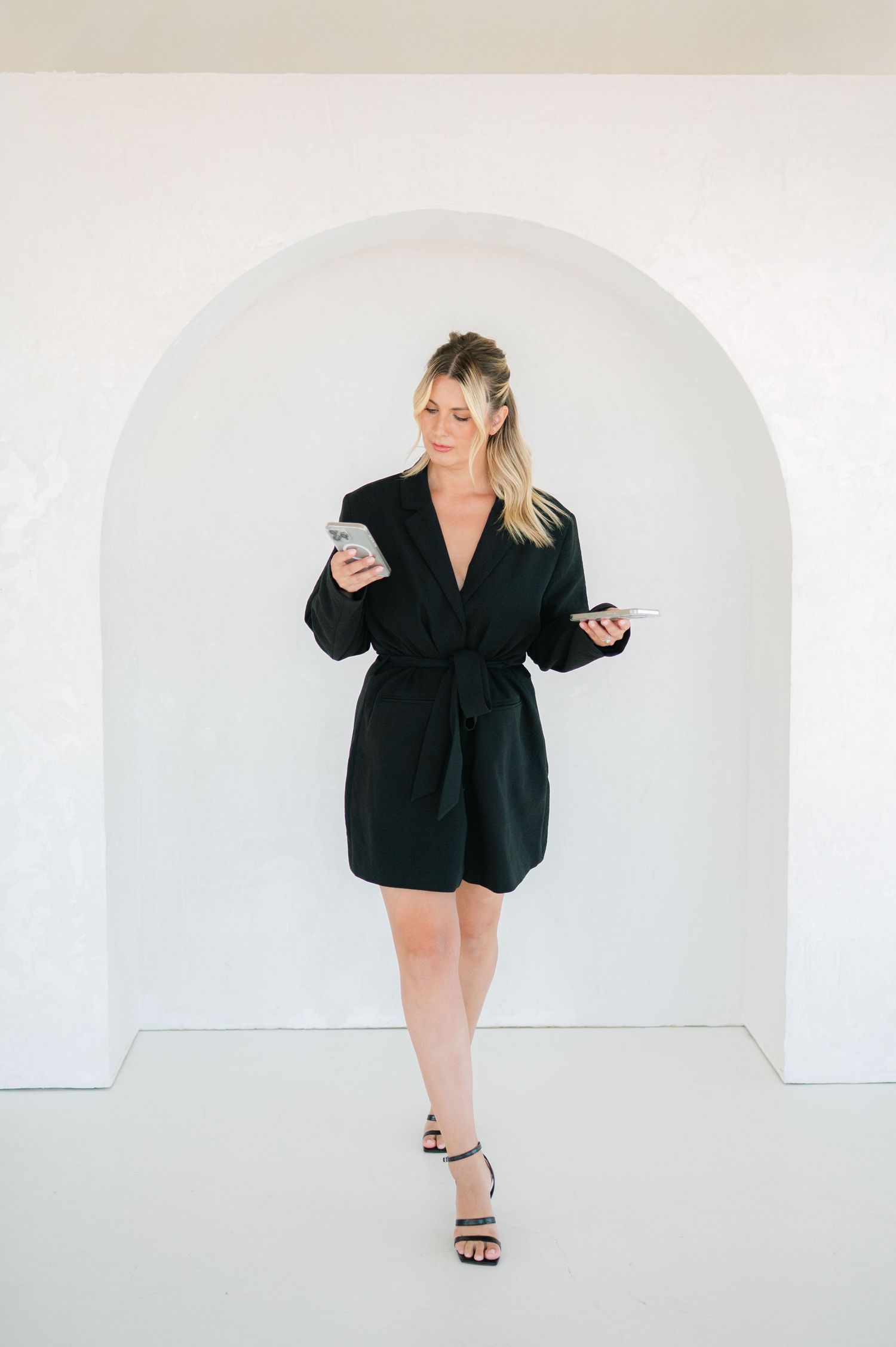 A person in a black blazer dress and heels poses against a white wall in a series of dynamic fashion shots.