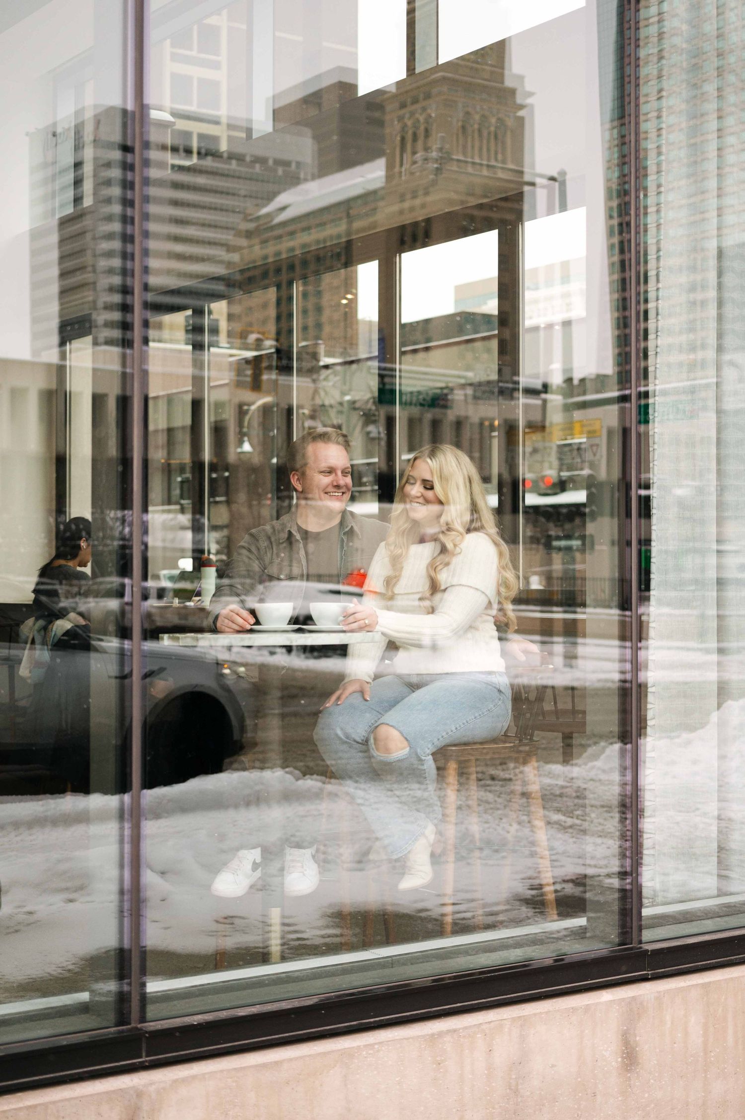 A casual cafe date scene photographed through reflective windows with urban architecture.