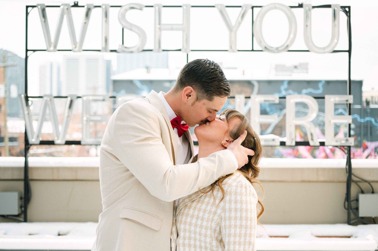 Couple embracing under 'WISH YOU' sign wearing matching cream and white formal attire.