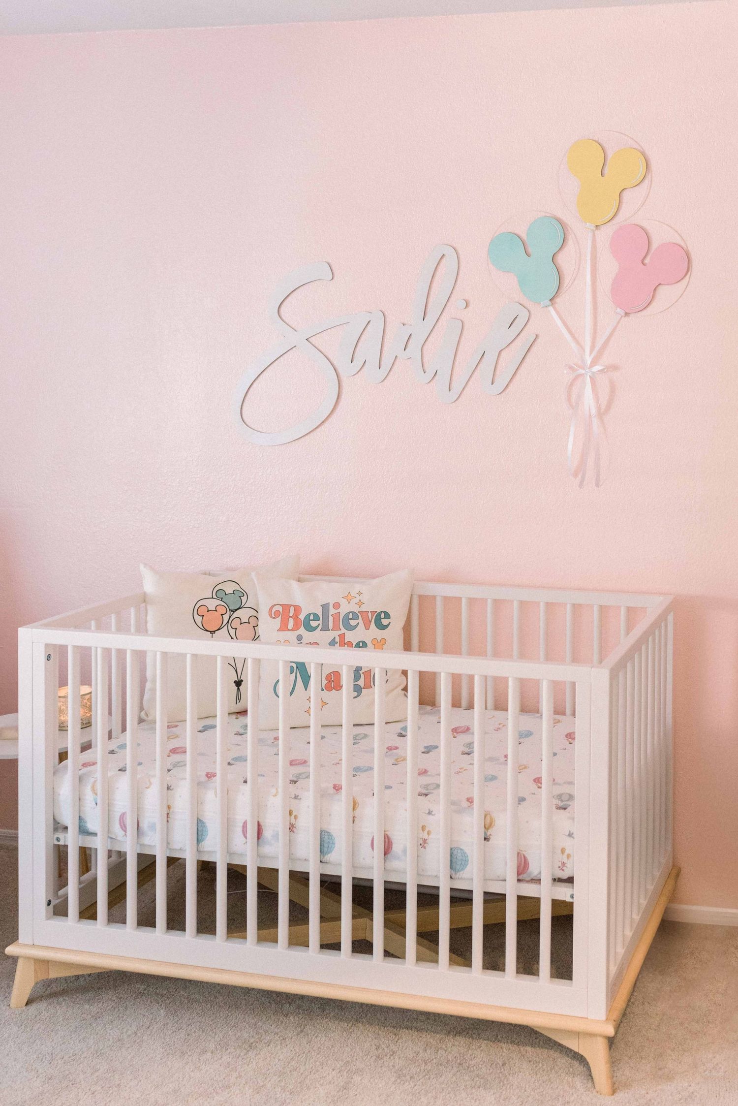 Modern white crib with Disney-themed decor in a pink nursery.