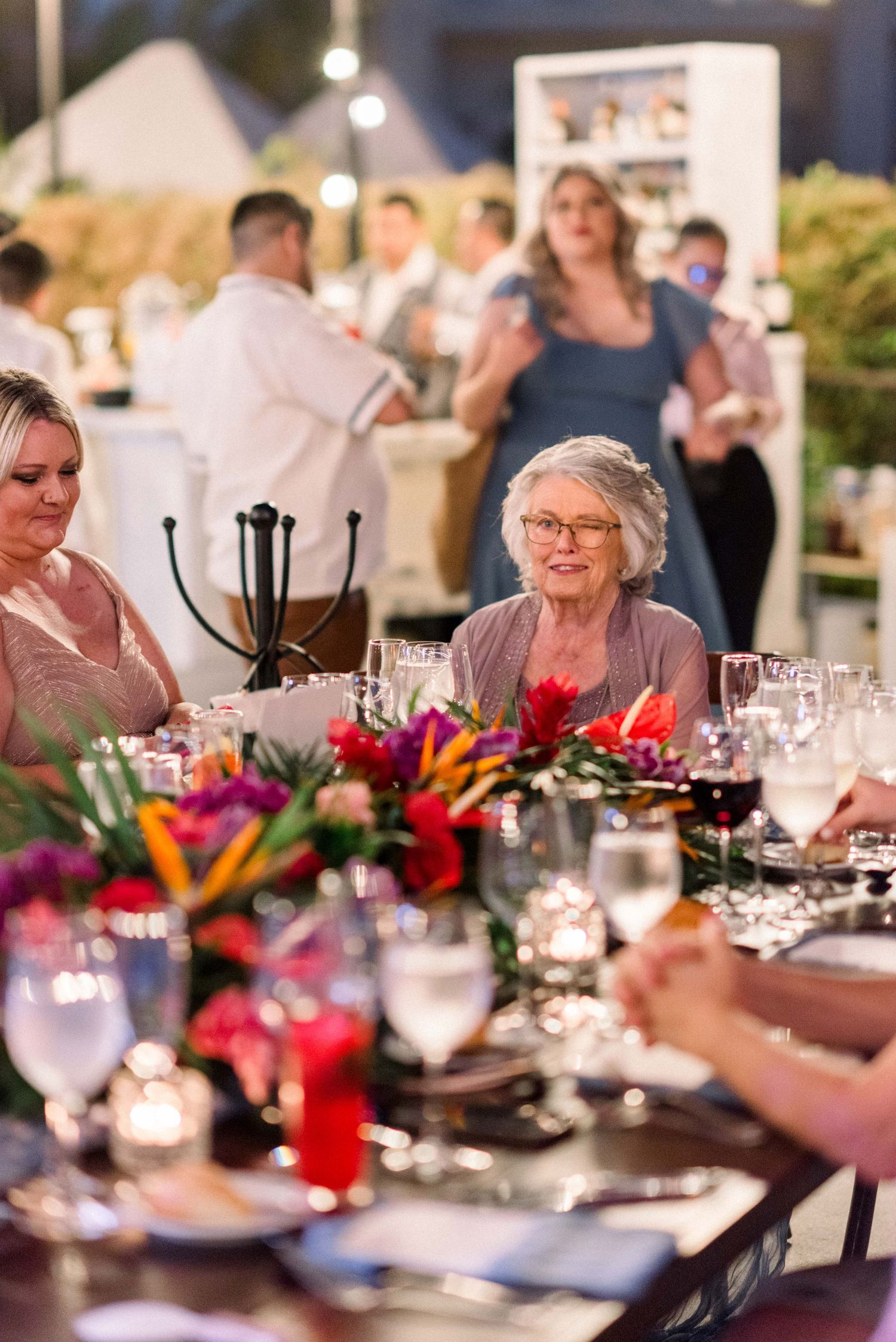 Elegant dinner table setting with vibrant floral centerpieces and candles at evening reception.