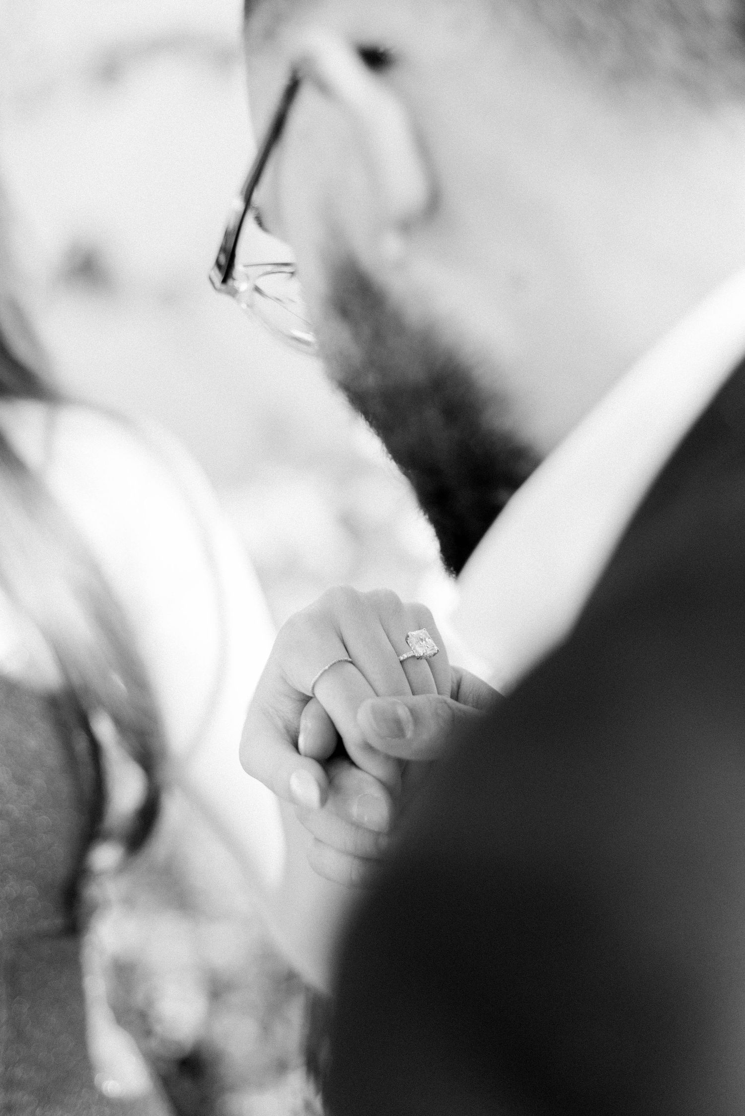 Close-up black and white photo showing hands and engagement ring during an intimate moment.