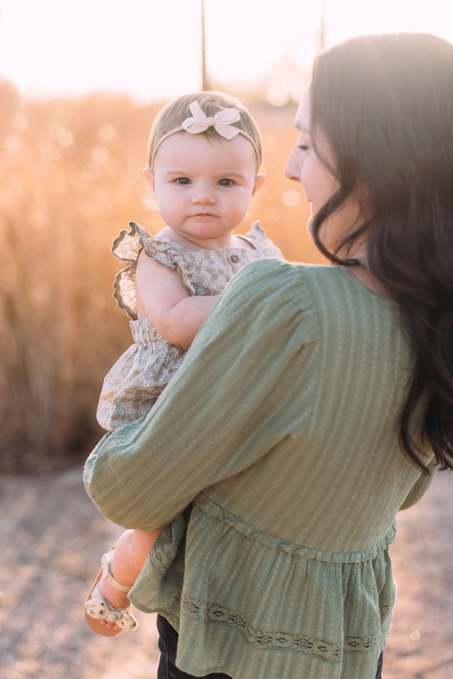 Sunset portrait with baby in floral dress and gray bow headband.