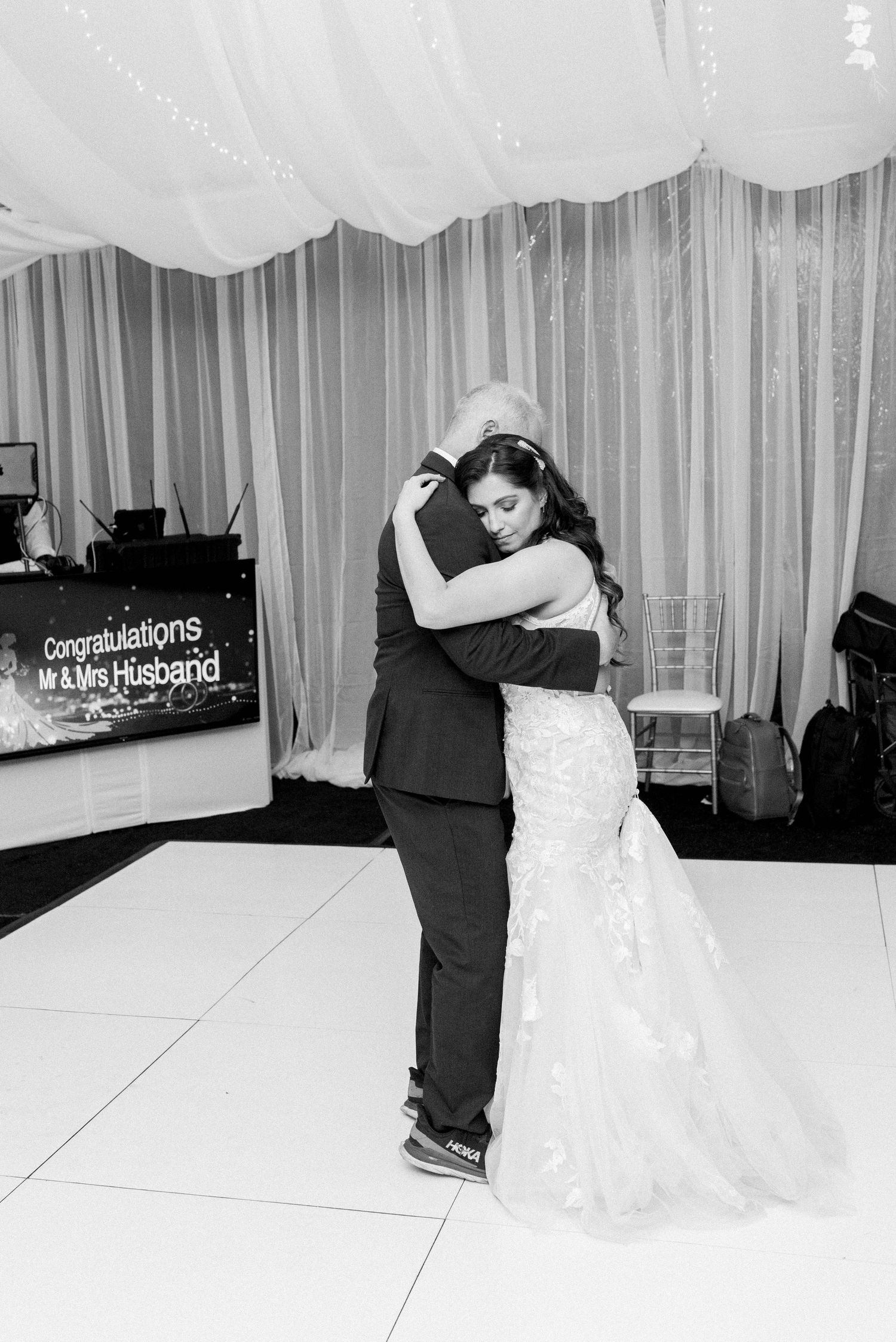 Black and white photo of couple embracing during wedding dance on white dance floor.