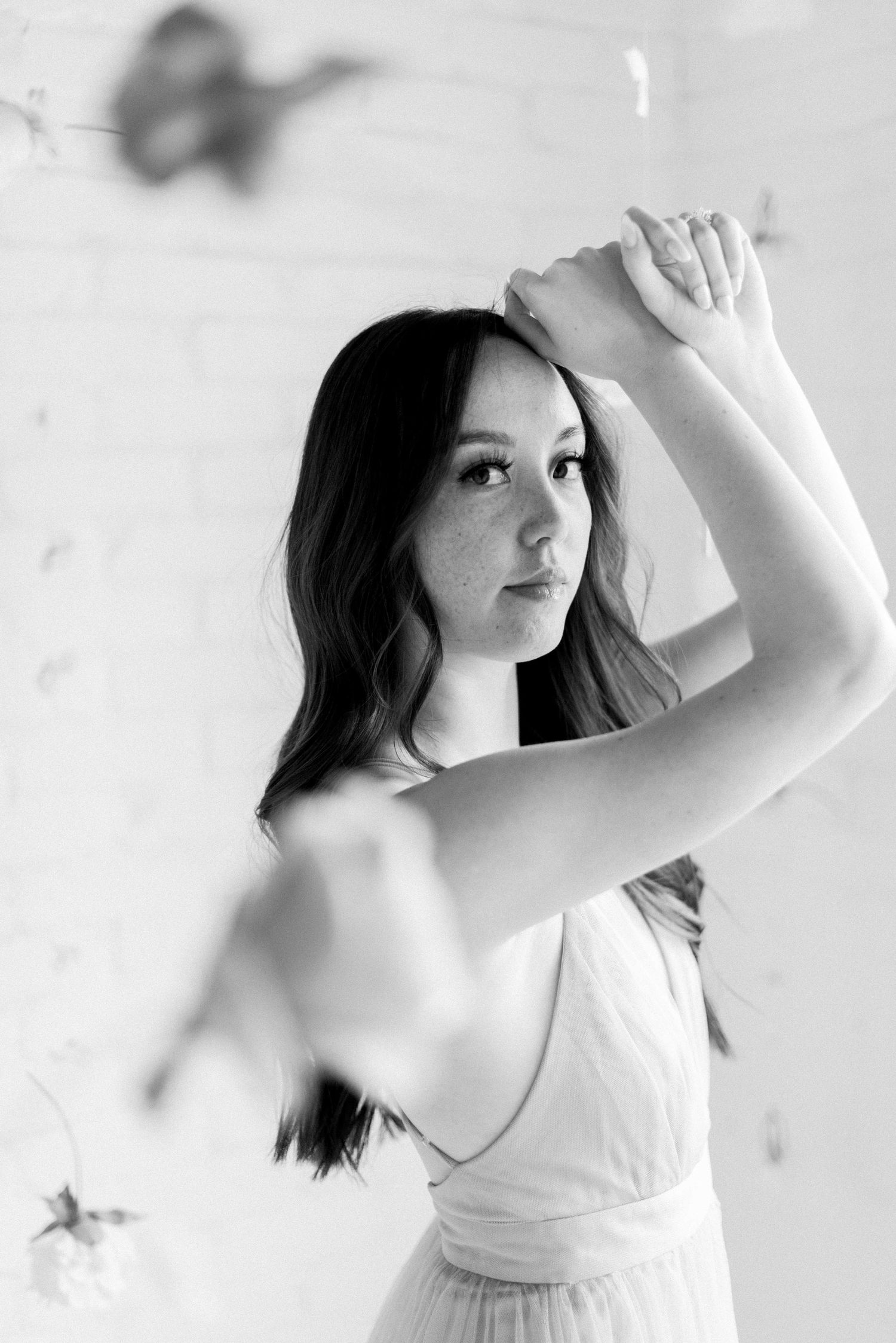 Black and white portrait showing graceful pose with raised arms and flowing dress.