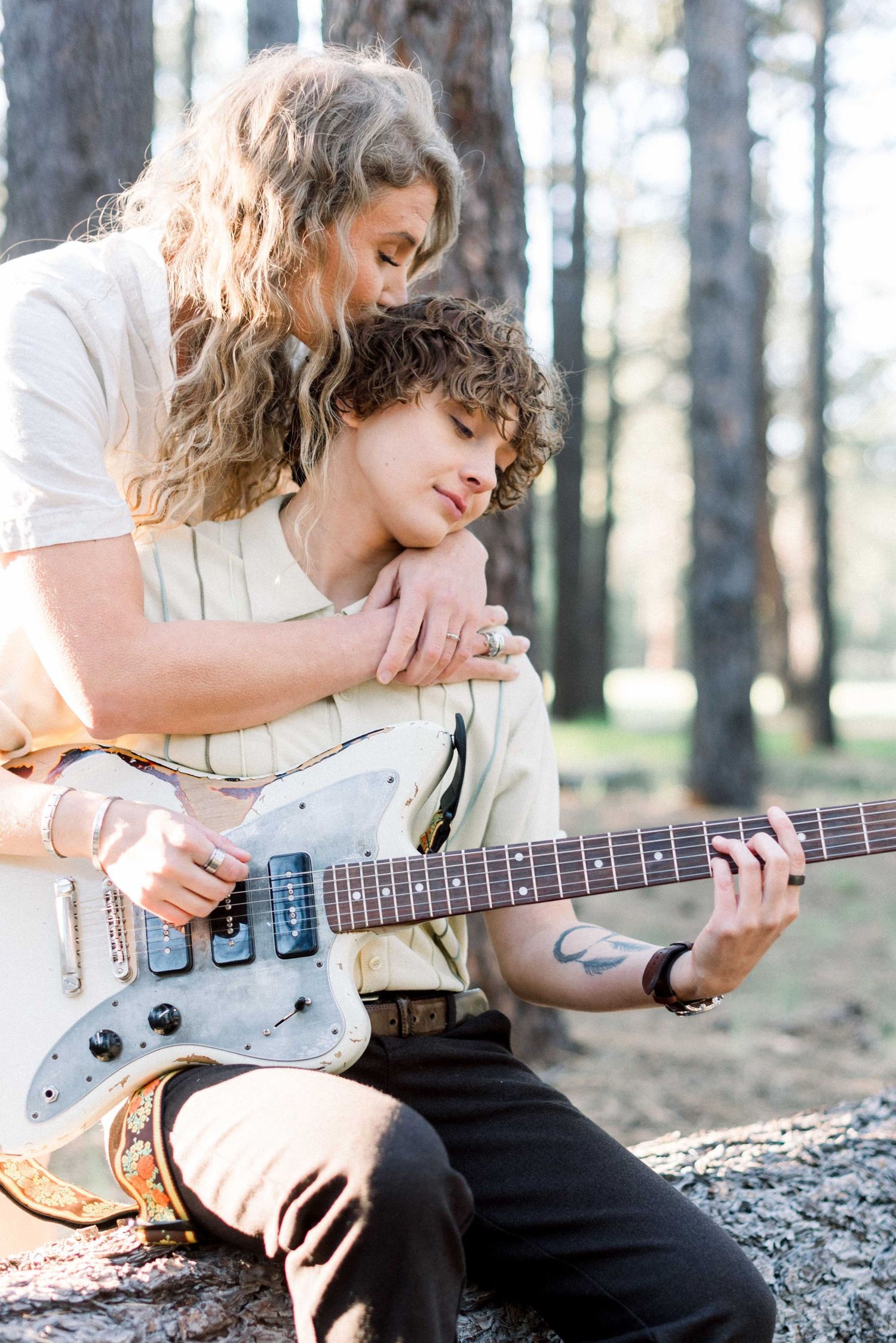 A romantic couple shares an intimate moment while playing an electric guitar in a sunlit forest setting.