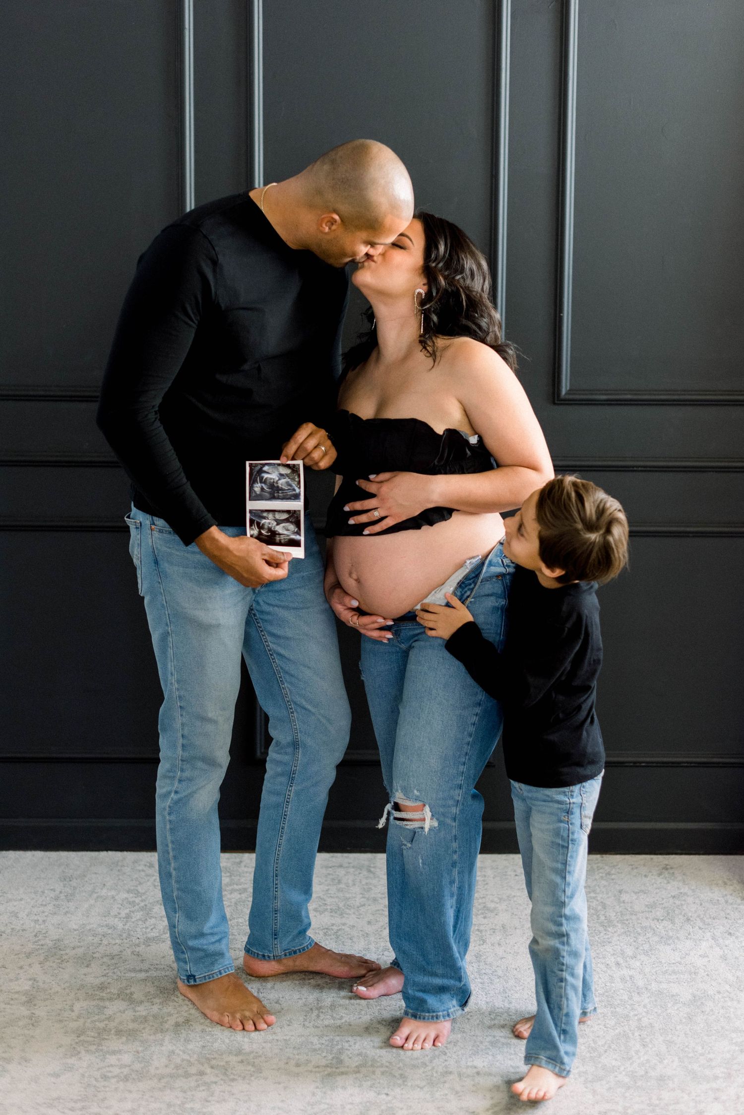 Intimate family moment sharing ultrasound photo against dark paneled backdrop.