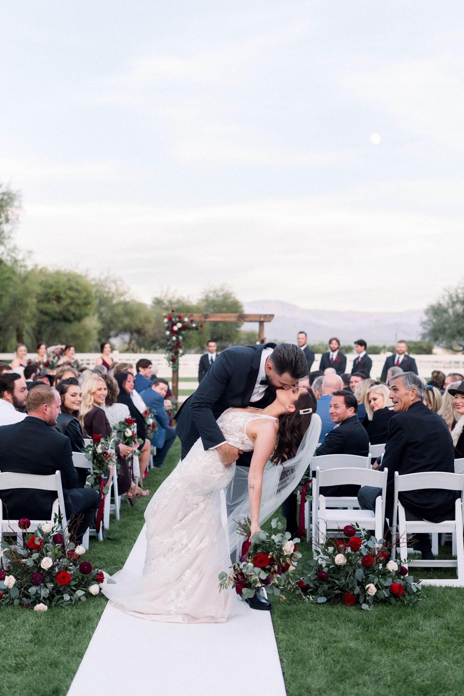 A dramatic dip kiss on a white aisle runner during an outdoor wedding ceremony.