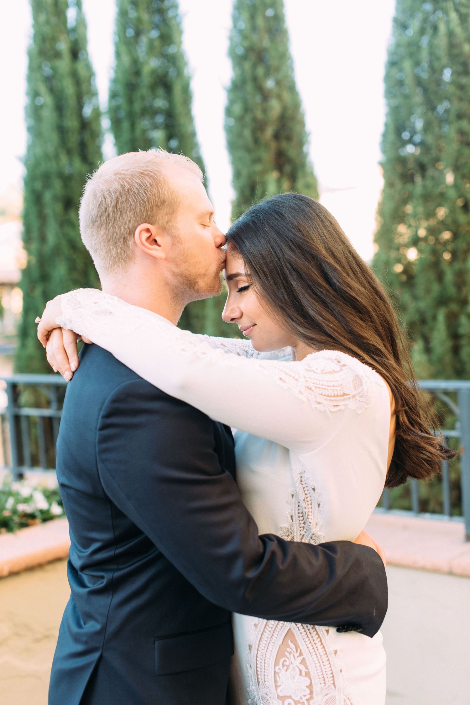 A romantic embrace between newlyweds with cypress trees in the background.